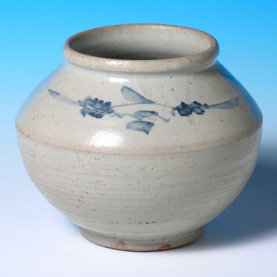 Korean ceramic storage jar, thickly potted with slanted shoulder decorated in under glaze cobalt blue of blossoming sprays, simple rolled lip and footed base, glazed overall in a translucent glaze except for the orange biscuit foot rim with some