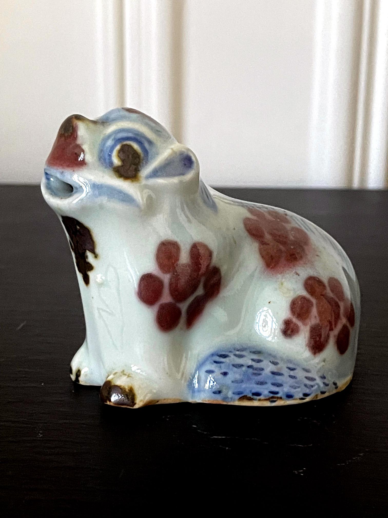 A lovely Korean ceramic water dropper in the form of a sitting dog circa 19th century late Joseon Dynasty. The charming animal form features underglaze blue paint outlining the furs along the spines and legs and iron red cluster markings scattered
