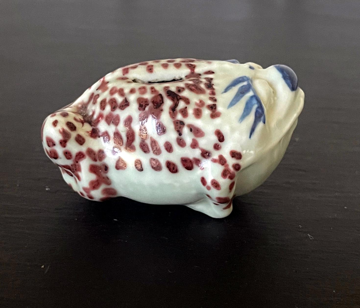 A Korean ceramic water dropper in the form of fog circa early 20th century likely from Japanese colonial time post 1910s. The animal form features underglaze blue paint and iron red dotted markings covering the body. The rendition was rather rustic