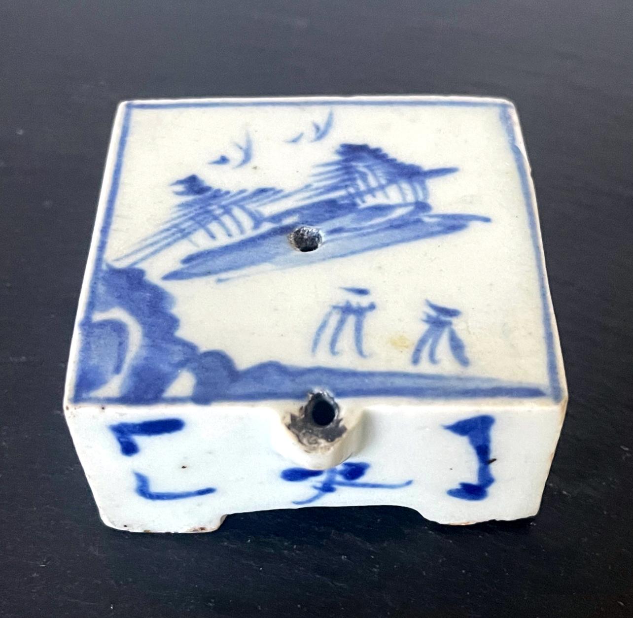 A small Korean ceramic water dropper in square form on four corner feet, circa 19th century late Joseon Dynasty. The piece features an underglaze blue painting of a landscape with mountains and sailing boats on water, set on white glazed background.