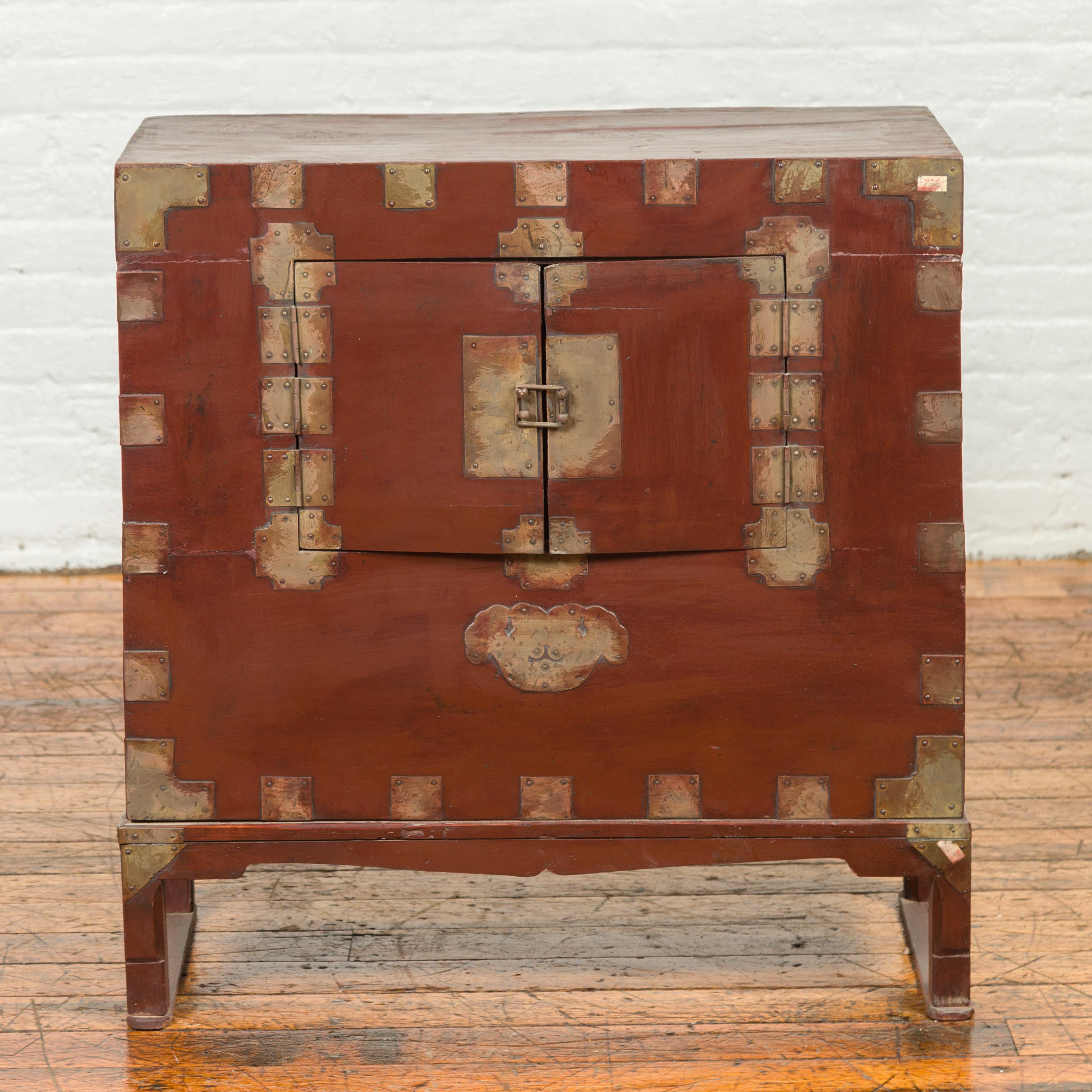 An antique Korean side chest from the early 20th century, with petite double doors and traditional brass hardware. Delve into the understated elegance and functional design of this early 20th century Korean side chest, a piece that embodies the