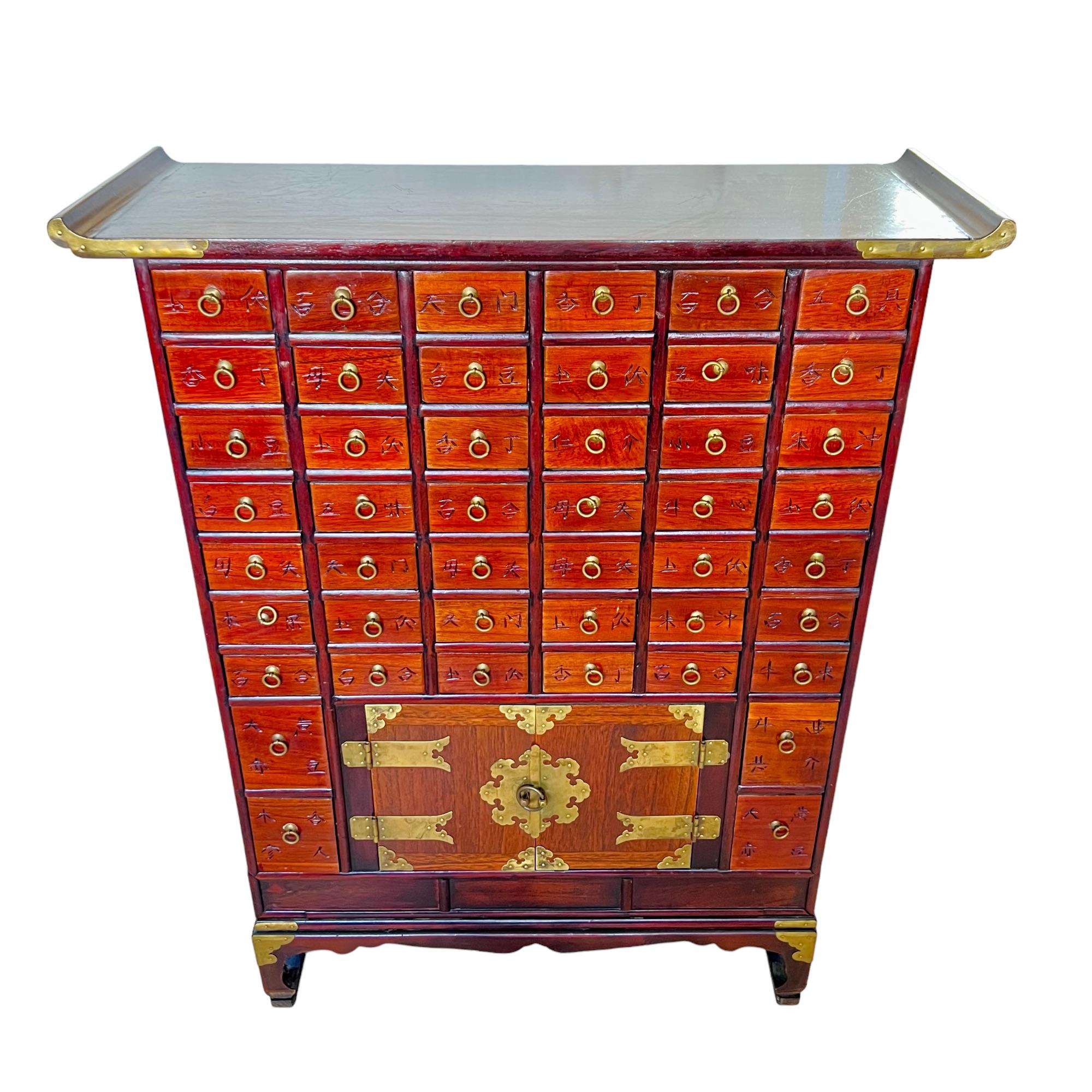 An early to Mid-20th century Korean elm and rosewood apothecary chest. This eye-catching medicine cabinet features a torii style rosewood top with brass mounts and boasts a total of forty-eight elm wood drawers - forty-four upper, four middle and