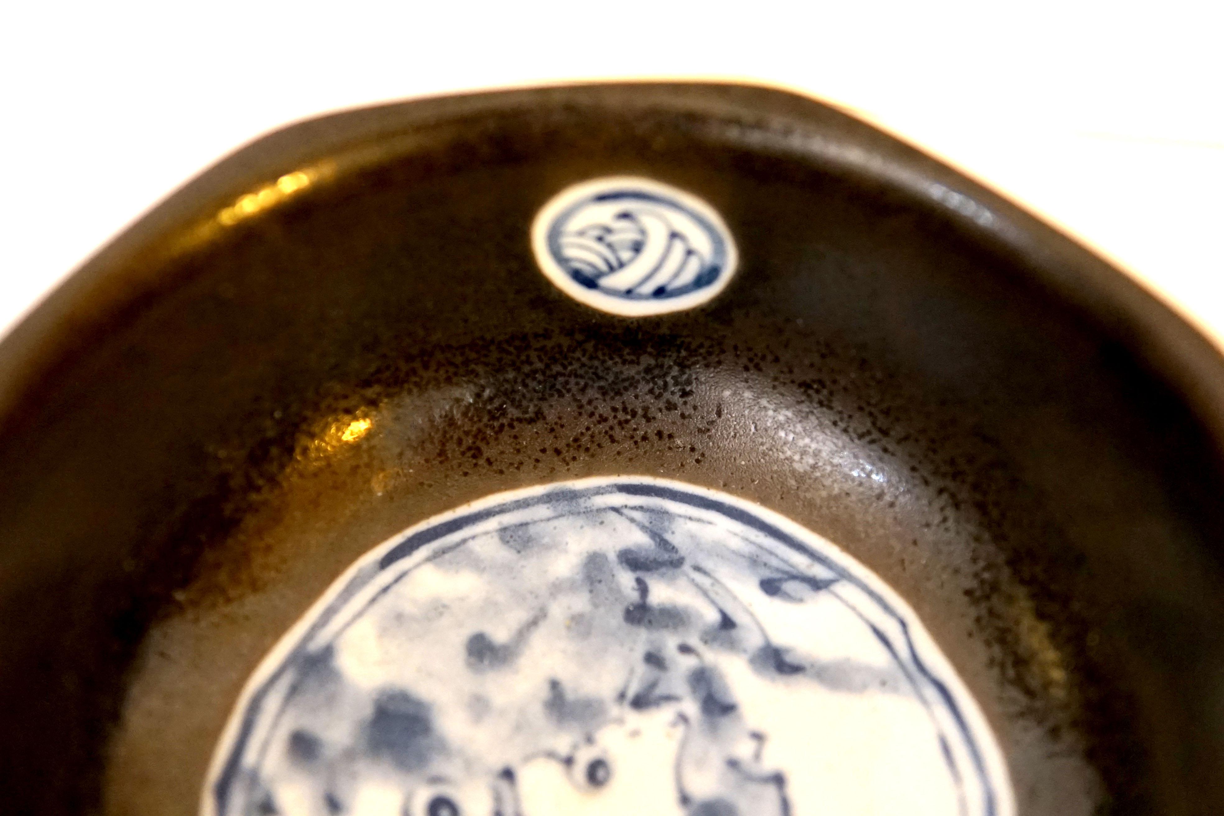 A small vintage Korean black glazed and blue and white octagonal faceted earthenware bowl is probably from the mid 20th Century. The contrast between the dark brown glaze and the blue and white design is striking.
The bowl is of octagonal section,