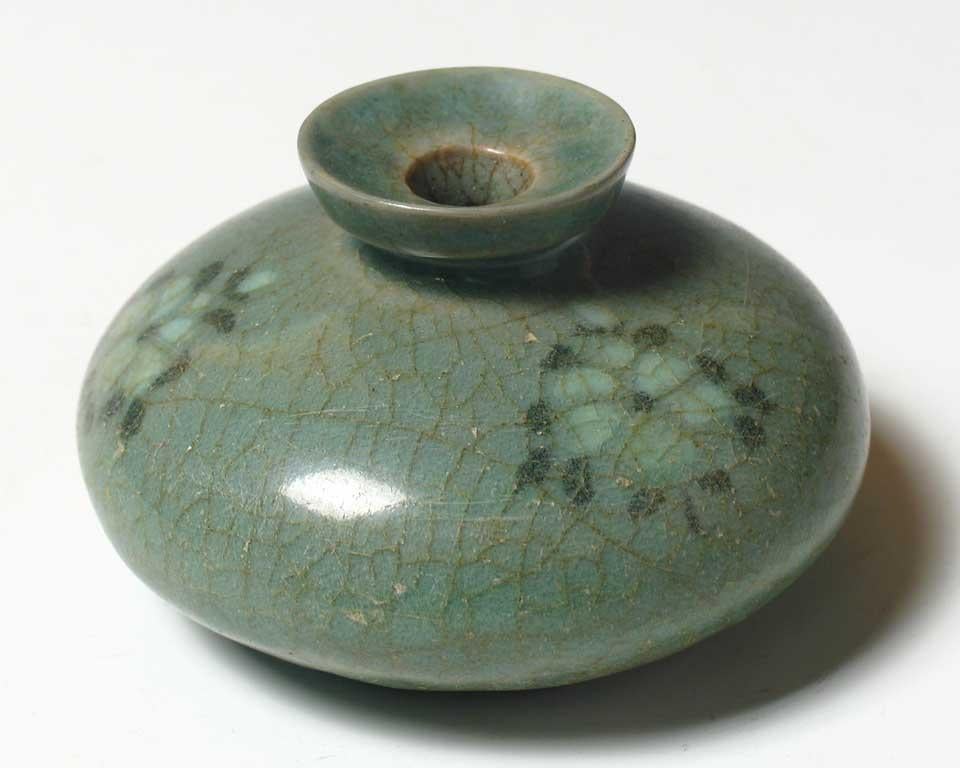 Korean inlaid ceramic celadon oil bottle, of compressed circular form inlaid in black and white slip of three flower blossoms on the shoulder, narrow neck, wider concave mouth rim, circular base with three spur marks covered overall in a transparent