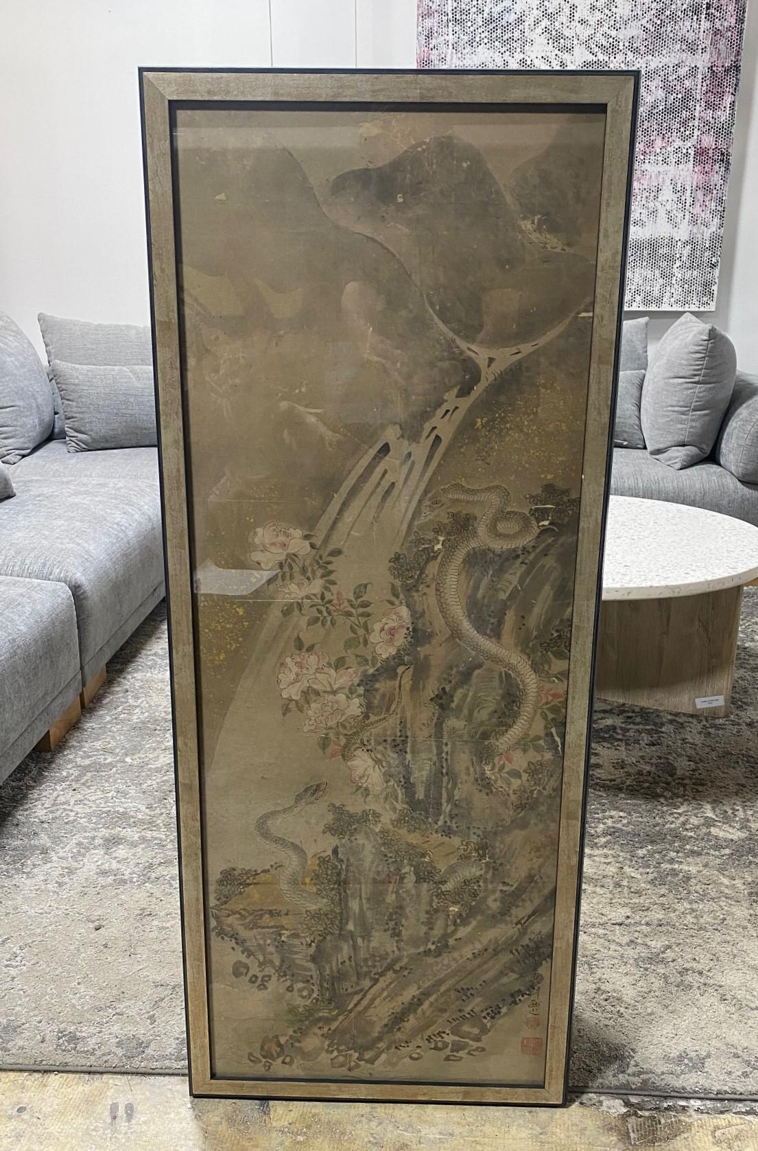 A beautiful and striking framed Japanese/ Asian serpent/snake scroll painting featuring two serpents/snakes in a garden landscape surrounded by blossoming and blooming flowers and a falling waterfall in the background. This work is hand-painted oil