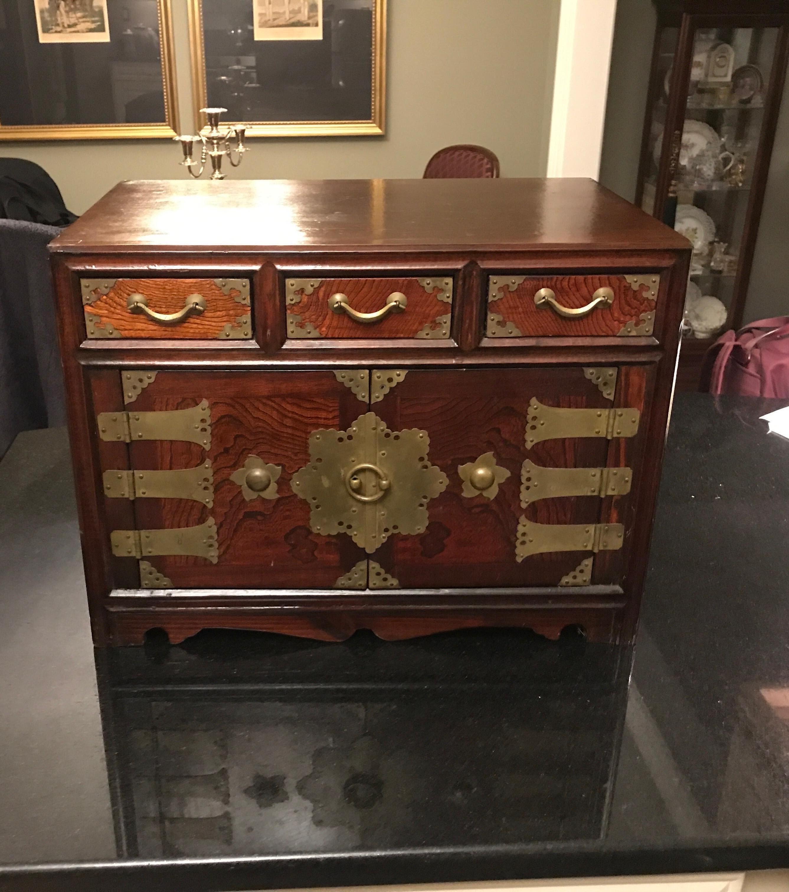 A Korean hardwood diminutive chest with brass mounts. The two doors open to reveal storage and drawers with three drawers along the top. The highly figurative wood on the front door and drawer panels with a slightly darker top and sides.

Measures: