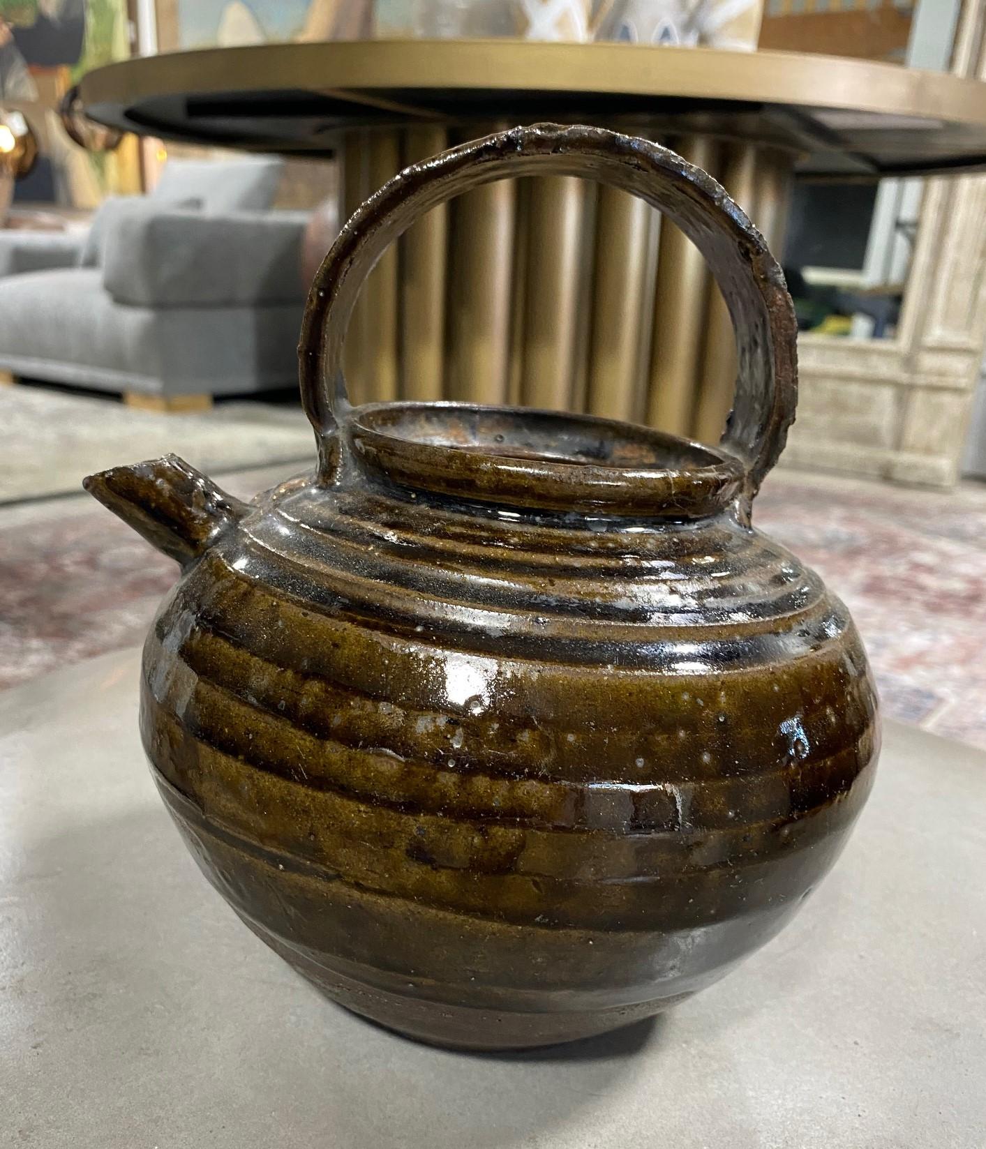 A wonderfully crafted Korean stoneware pottery teapot with a beautiful muted green and brown glaze, color, and nicely aged patina. This work radiates in the light.
We believe this piece is from the Joseon Dynasty (1392-1897) but as this is not our
