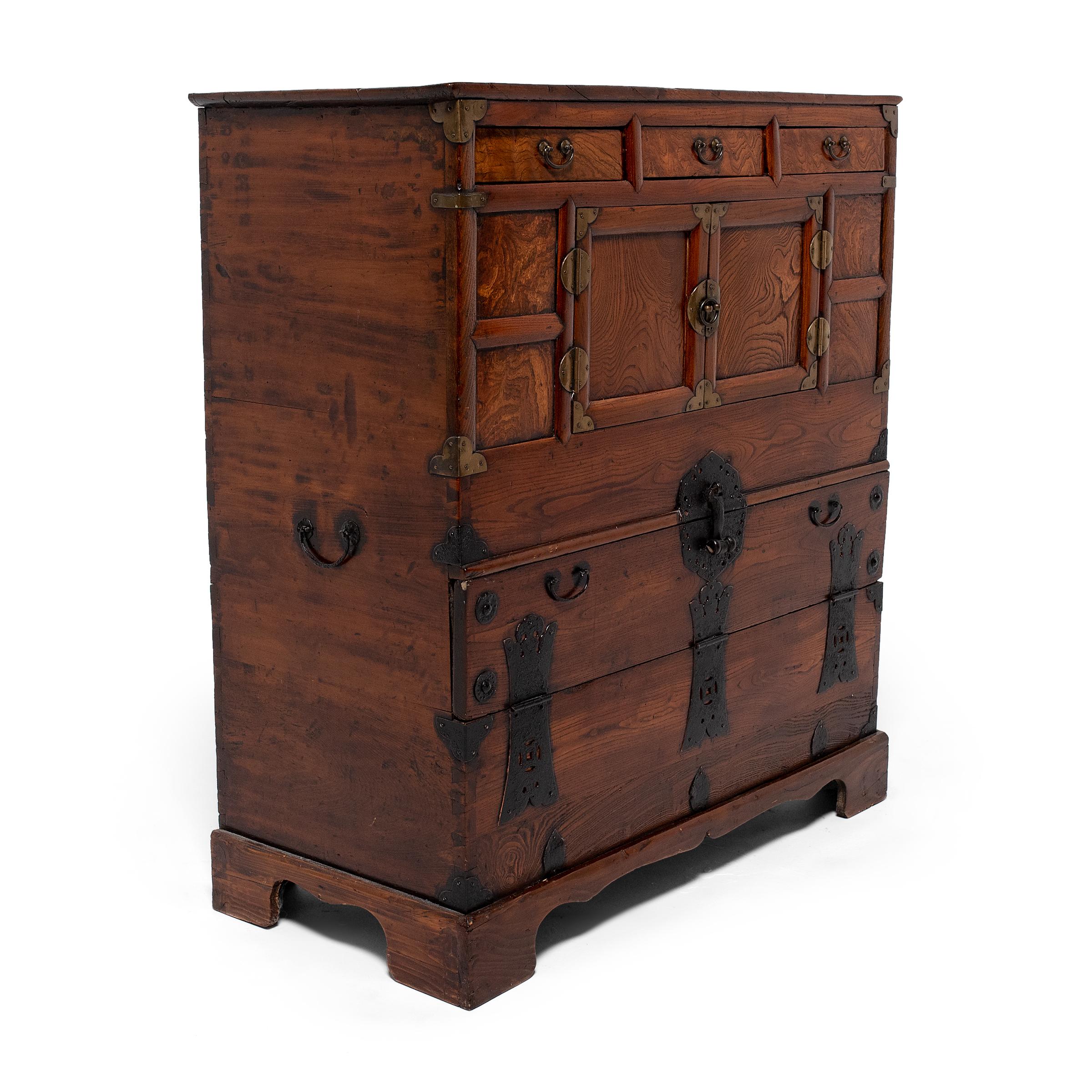 This early 20th century Korean cabinet was modified at some point in its life to combine a two-door paneled wardrobe (jang) with a low blanket chest (pandaji). The wardrobe was used to store clothing in a women's quarters, and the chest was used