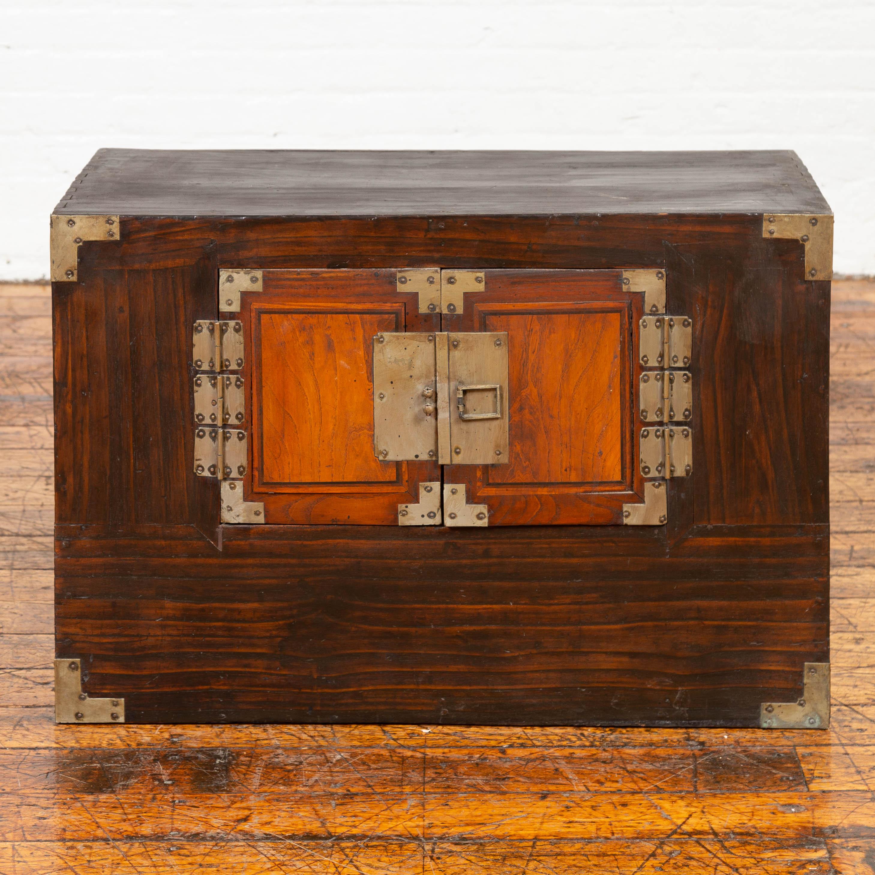 A Korean wooden two-toned side chest from the late 19th-early 20th century, with double doors and brass hardware. This Korean cabinet features a rectangular top sitting above a two-toned façade, made of petite double doors, accented with brass
