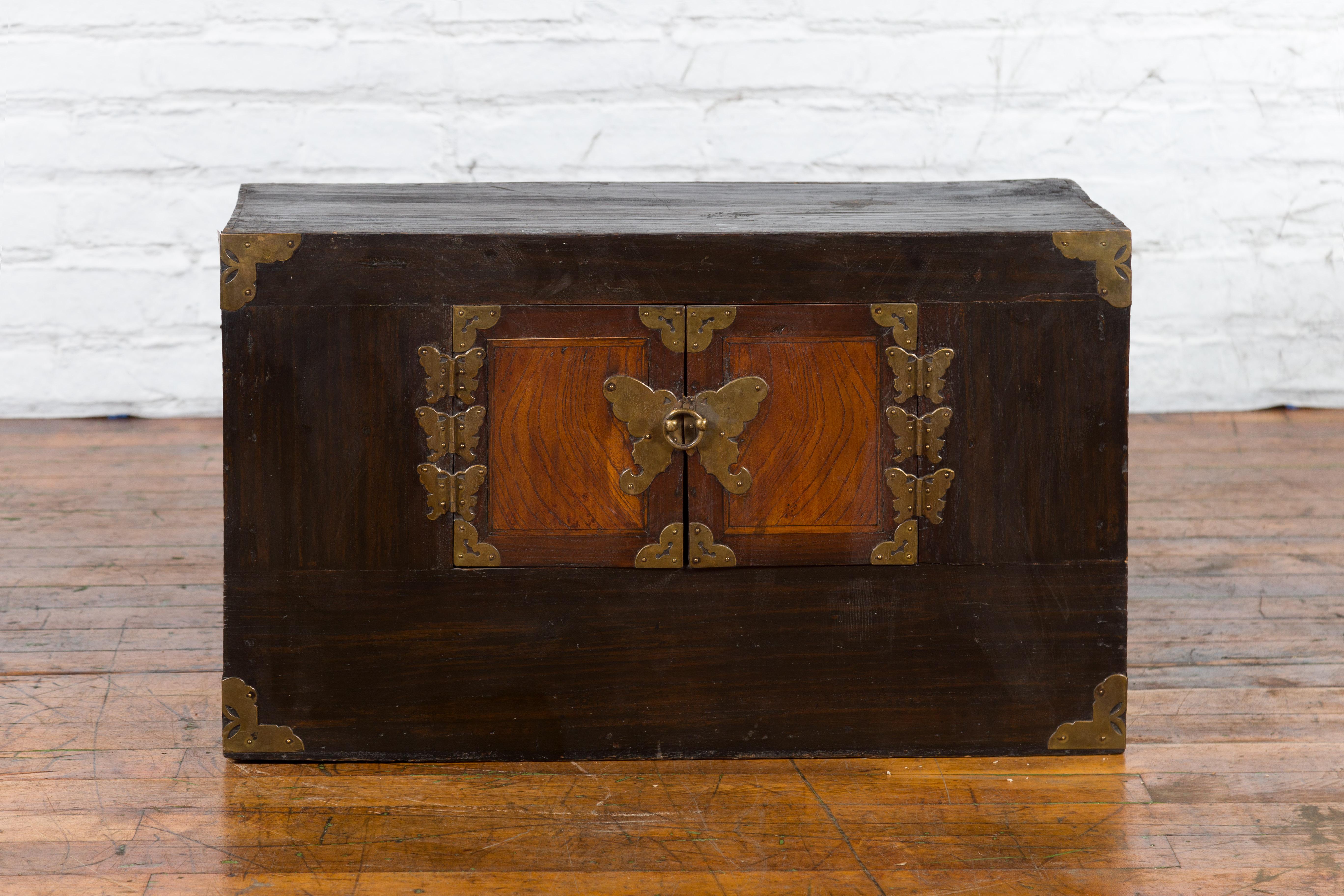 A Korean two-toned side chest from the late 19th century, with double doors and brass butterfly-shaped hardware. Created in Korea during the later years of the 19th century, this small cabinet features a rectangular top sitting above a two-toned
