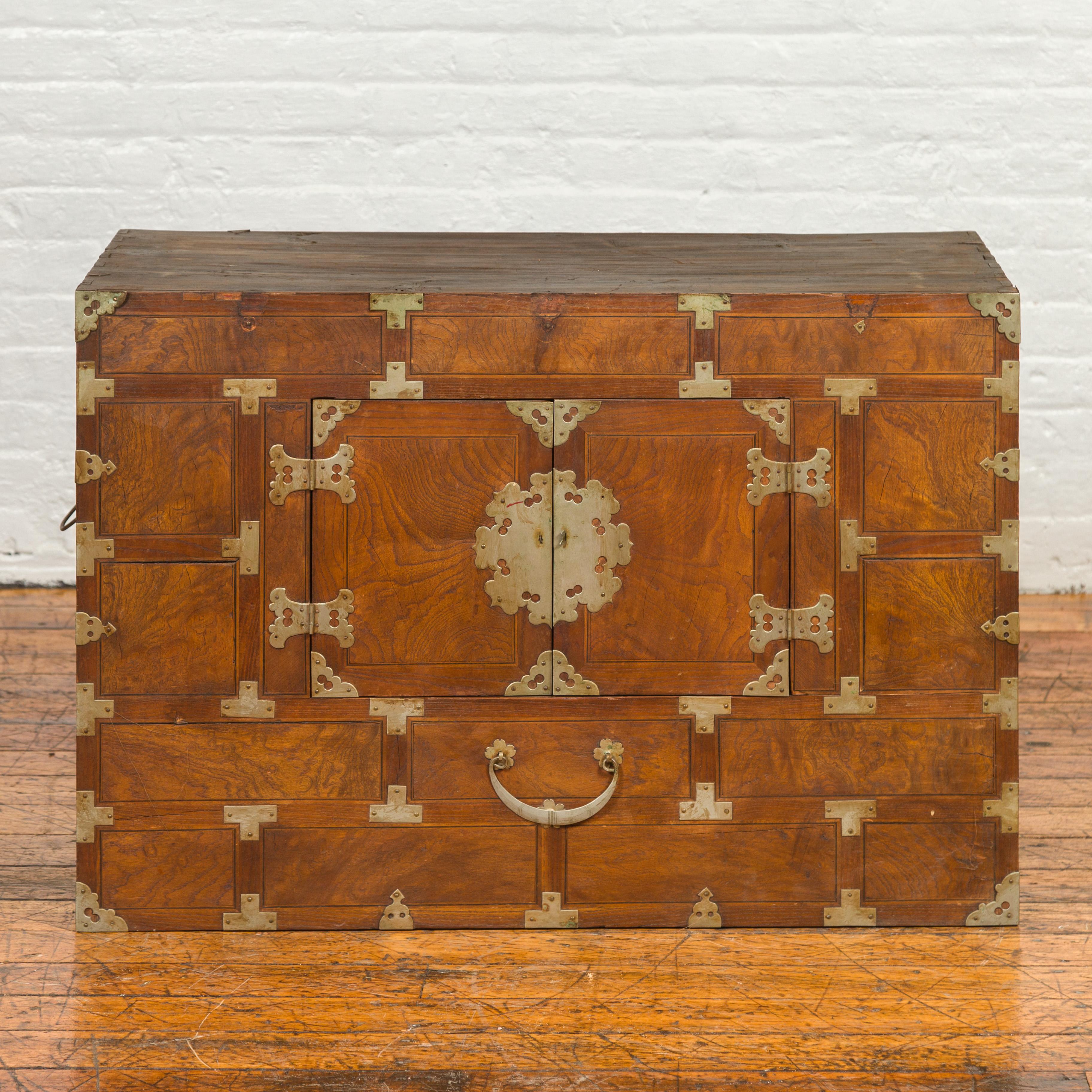 A Korean wooden side cabinet from the early 20th century, with double doors, abundant brass hardware and round medallion lock. Experience the allure of Eastern simplicity with this early 20th century Korean side cabinet, a delightful fusion of