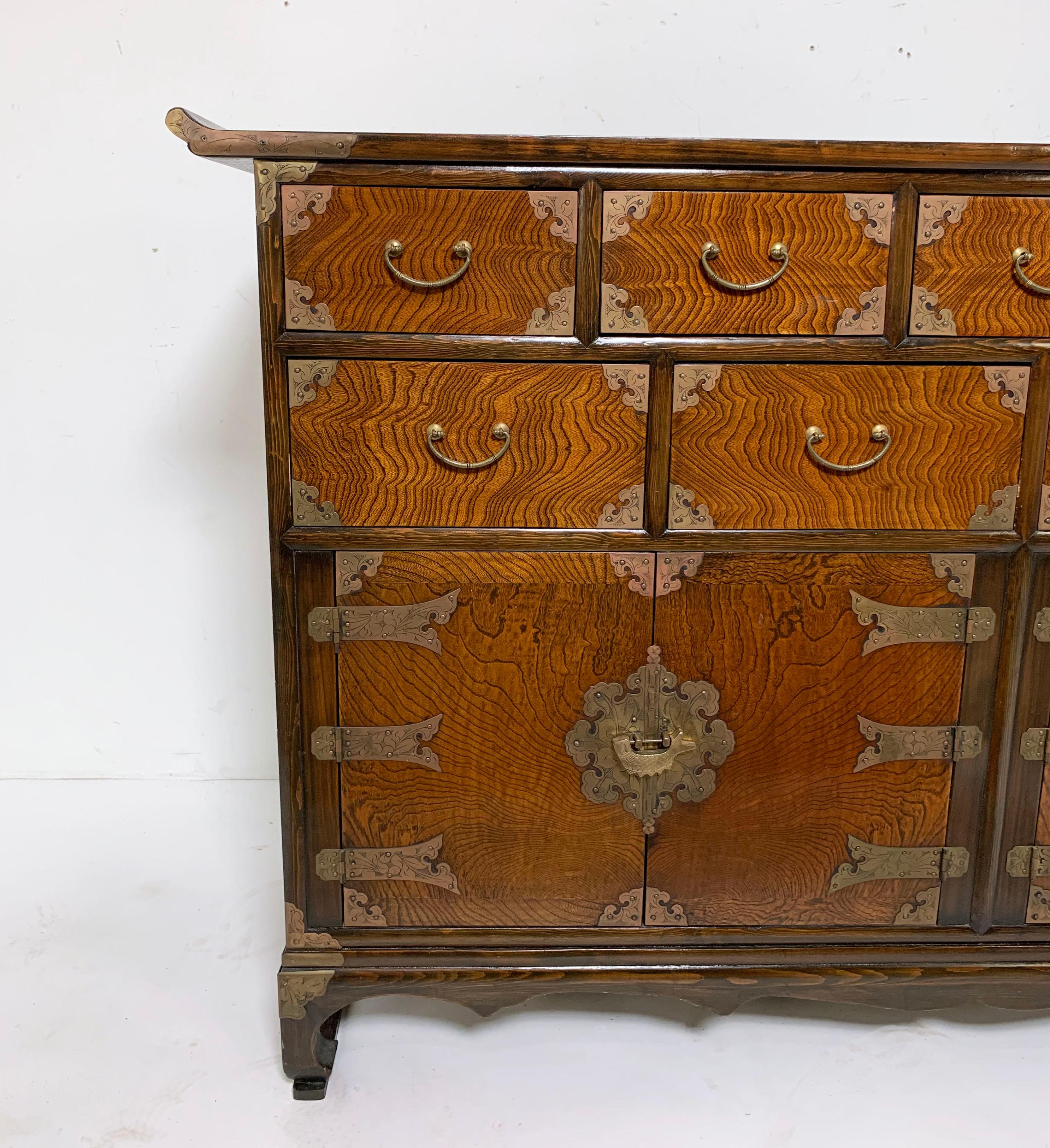 An elegant Korean tansu in elm and persimmon wood with chased brass hardware, consisting of nine drawers and two compartments below. This 59.25” wide chest is a fairly rare form not often seen in Korean cabinetry. Its broad configuration makes it