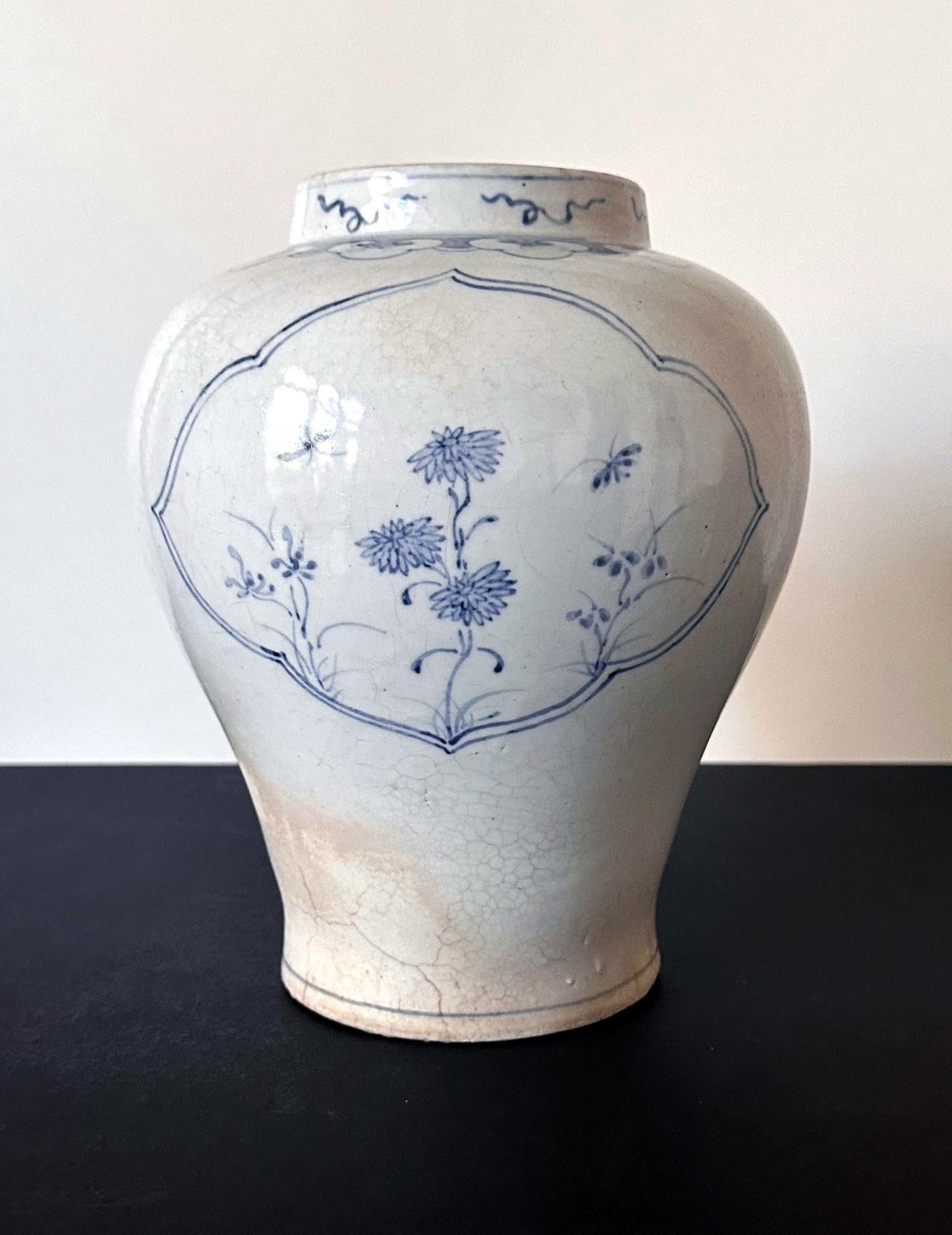 A Korean ceramic storage jar in the classic shape with broad shoulder, gently tapered body, a short neck with a large opening. The jar is covered in a white glaze and decorated with sparse but lovely underglaze blue paint. It was estimated to be