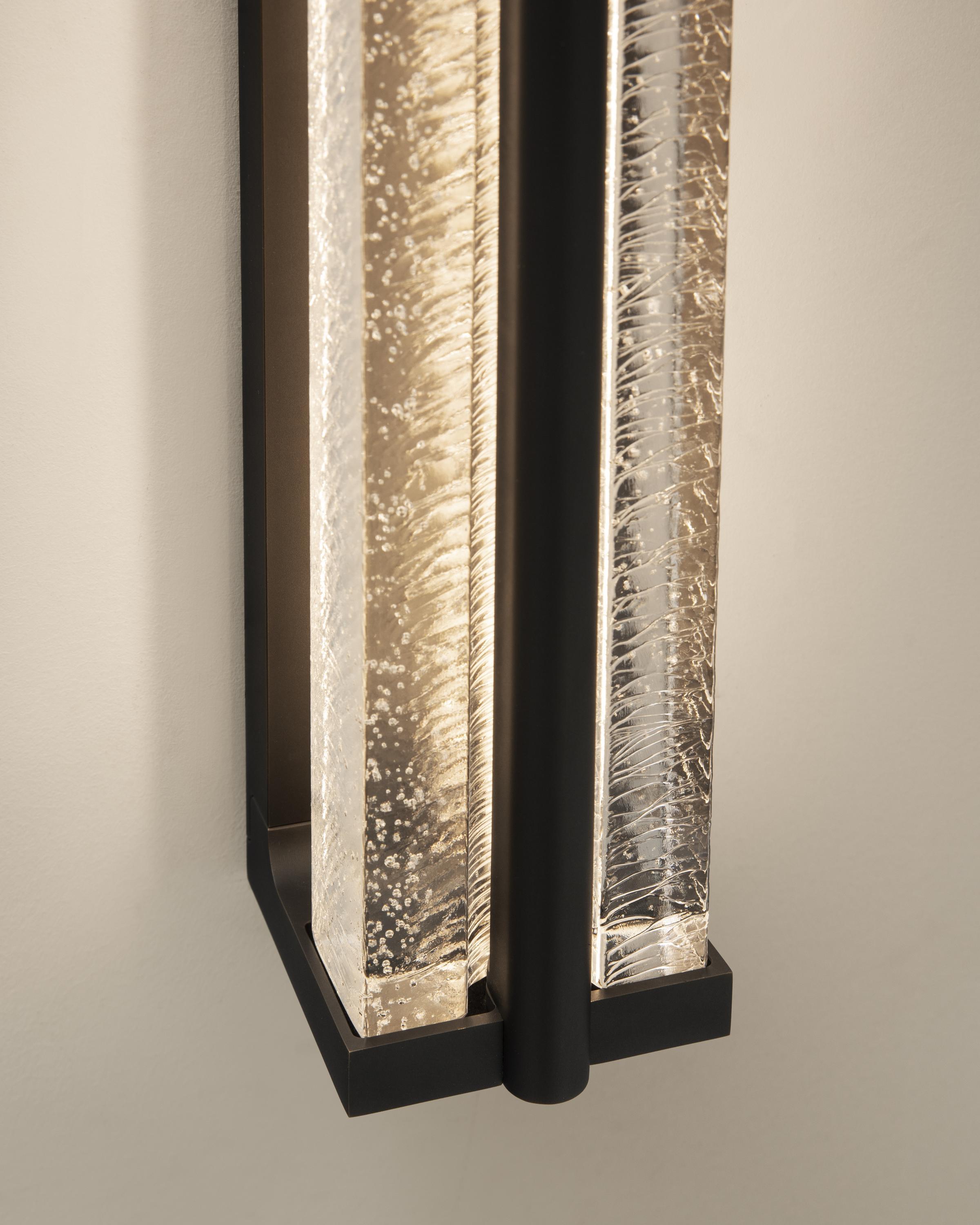 The wonderfully textured cast glass of the Kori Sconce emits a glow reminiscent of dripping icicles at night, inspiring its name which means “ice” in Japanese. These textures are complemented by a minimalist brass frame designed to support the glass