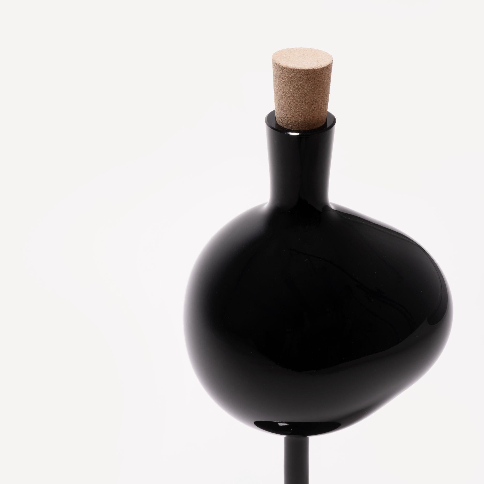 Like a tall wineglass, Bod balances confidently while its bowl captures the play of light. With their sheer and tall shape, the bottles are a piece of art that stands grounded in every home. The black glass bottle on a foot has an opaque surface and