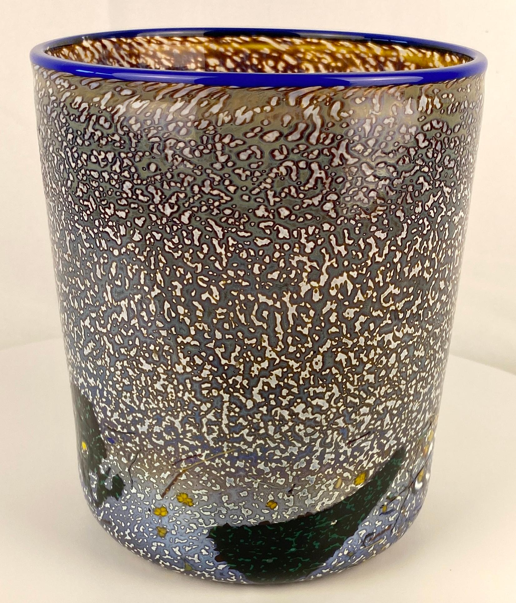 A lovely Kosta Boda glass vase or planter. The specked details makes this glass vase or planter very appealing accentuated by a purplish/blue rim. 
This decorative object is signed by the artist, Bertil Vallien and numbered. 

Place this Kosta Boda
