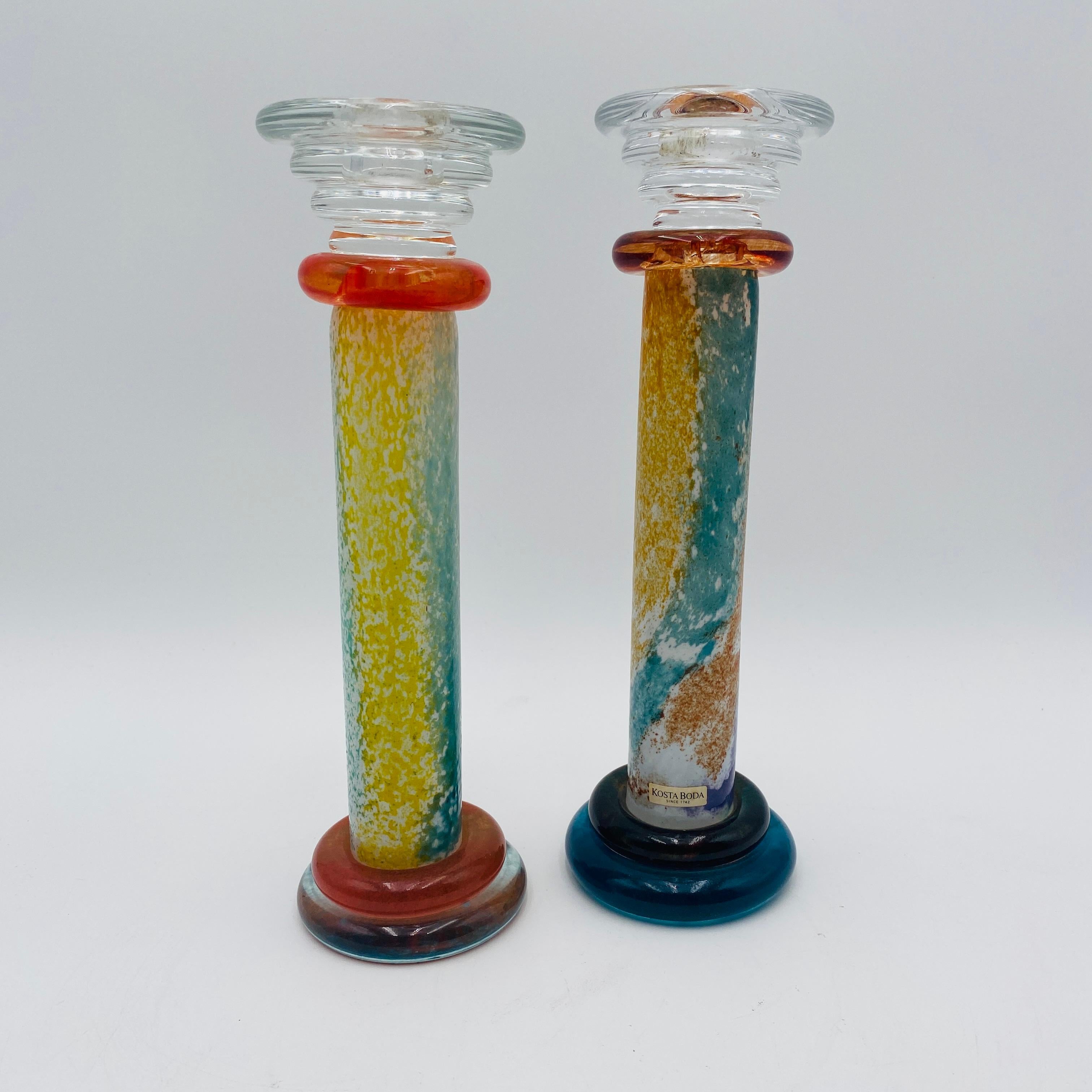 This is a set of 2 colorful candlestick holders from the Kosta Boda 'Can Can' series designed by Kjell Engman and made in Sweden. Features a multicolor glaze with donut shape accents. Each measures approximately 10” tall. Original Kosta Boda