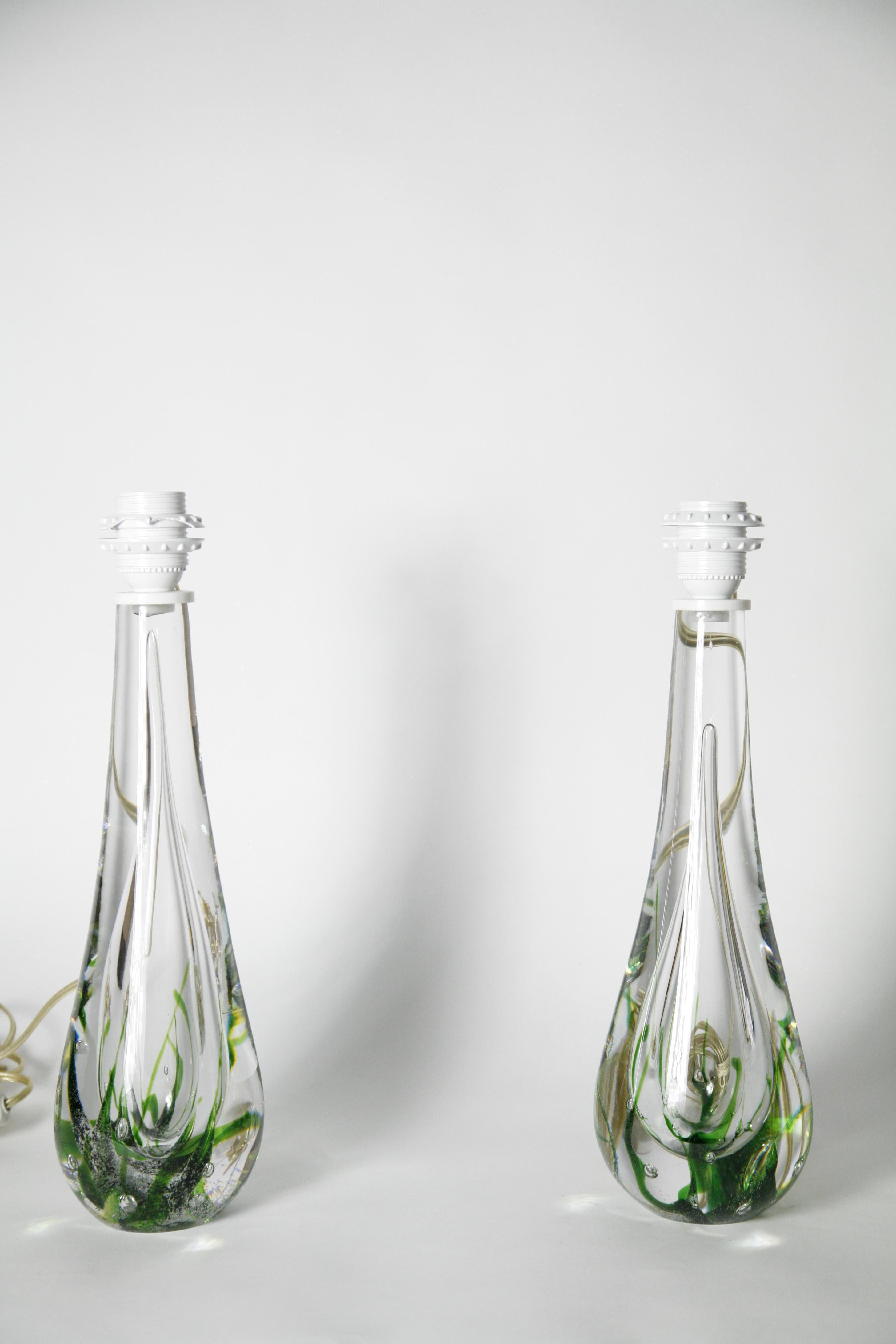Pair of solid clear glass lamps designed by Vicke lindstrand produced by the Swedish glassmaker Kosta 1980 Sweden signed clear crystal with air bubbles and green glass swirls inside the glass heavy solid bases. 
Measurement is for the glass base
