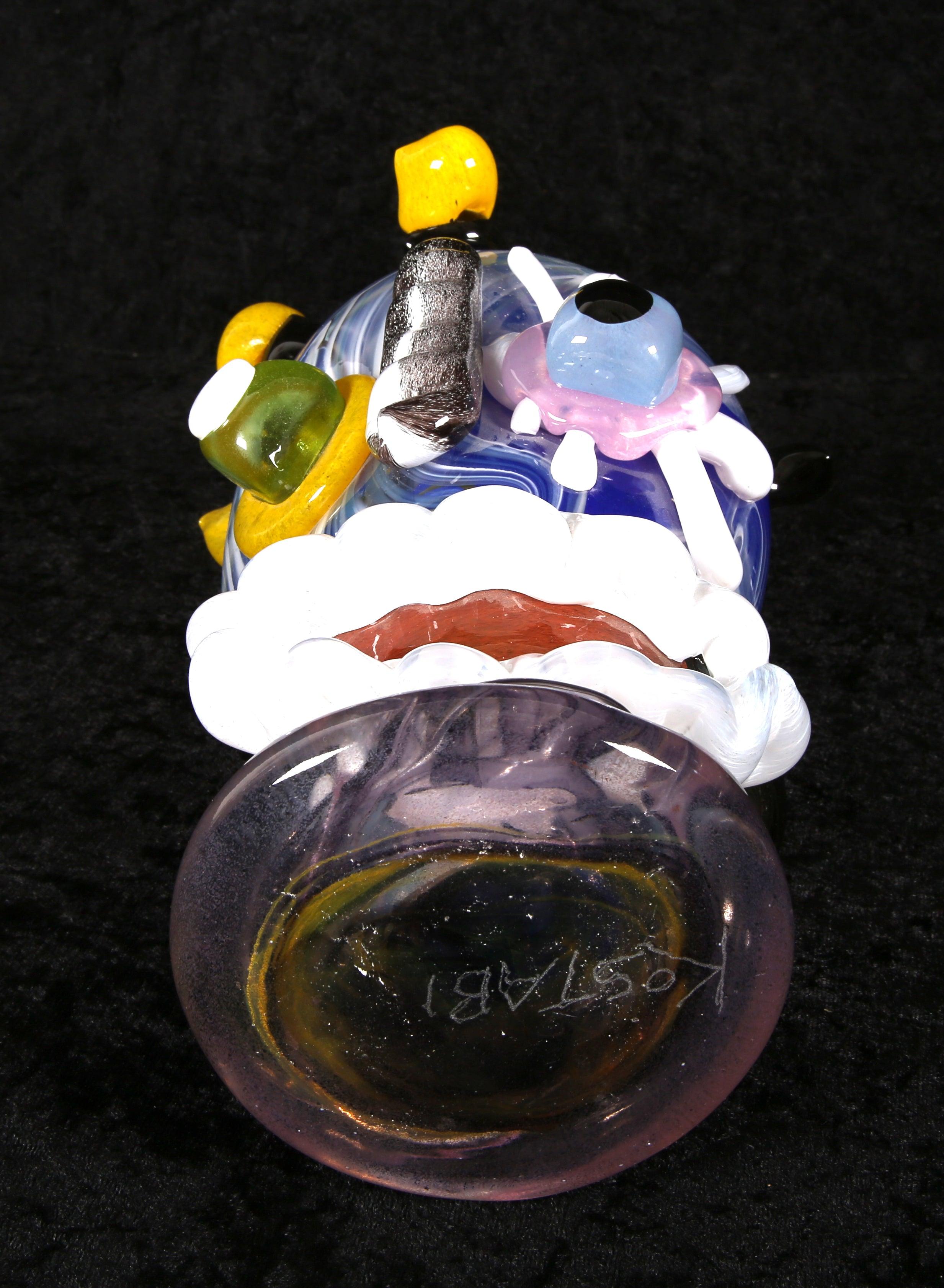 Esta singular escultura de cristal de Murano, obra de Paul Kostabi, es un ejemplo único de artesanía veneciana. Soplado a boca y cortado a mano en la Fábrica de Cristal Hofmeister de Amberg, es una obra verdaderamente única que presenta unas caras