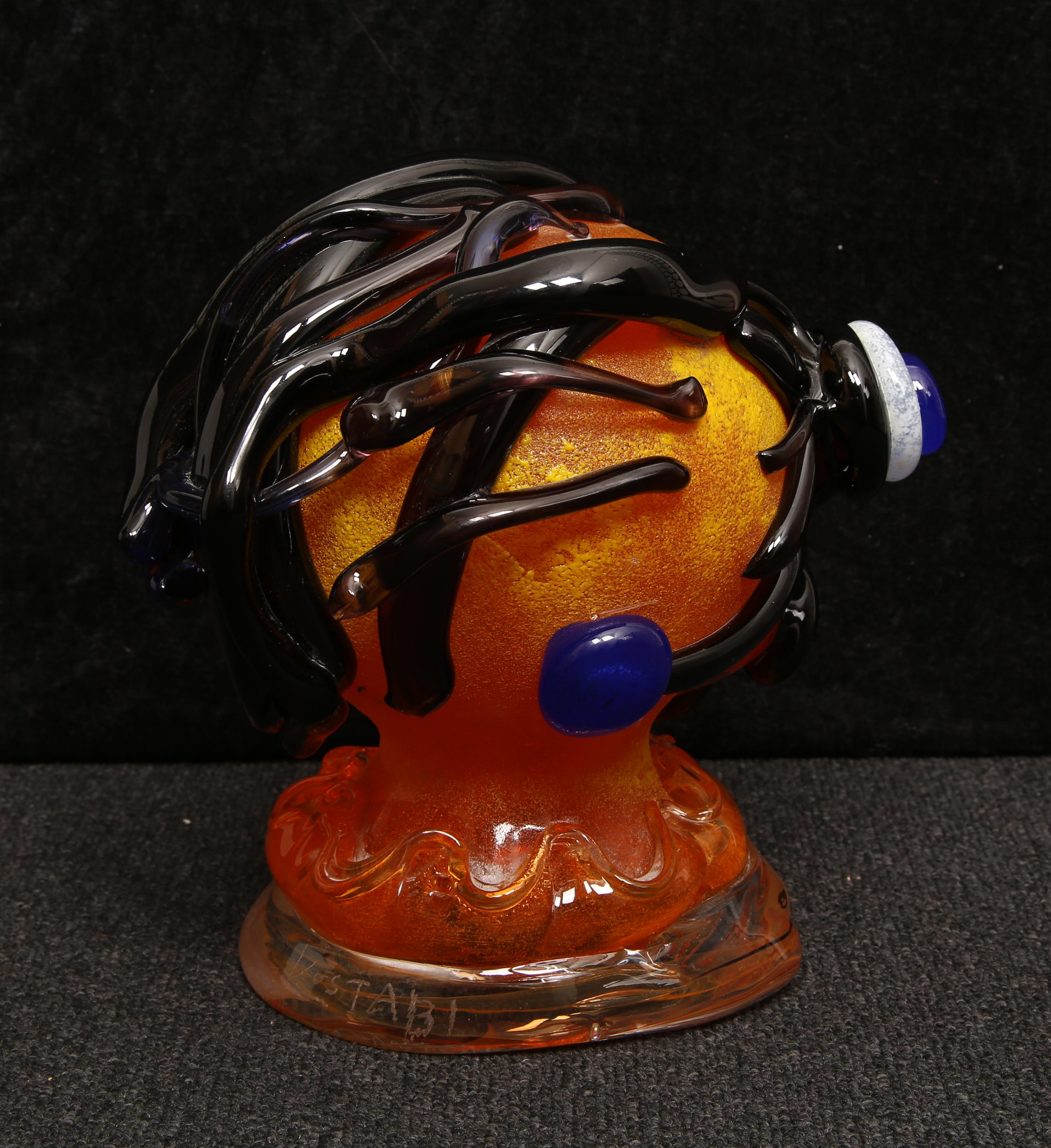 Esta singular escultura de cristal de Murano, obra de Paul Kostabi, es un ejemplo único de artesanía veneciana. Soplado a boca y cortado a mano en la Fábrica de Cristal Hofmeister de Amberg, es una obra verdaderamente única que presenta unas caras