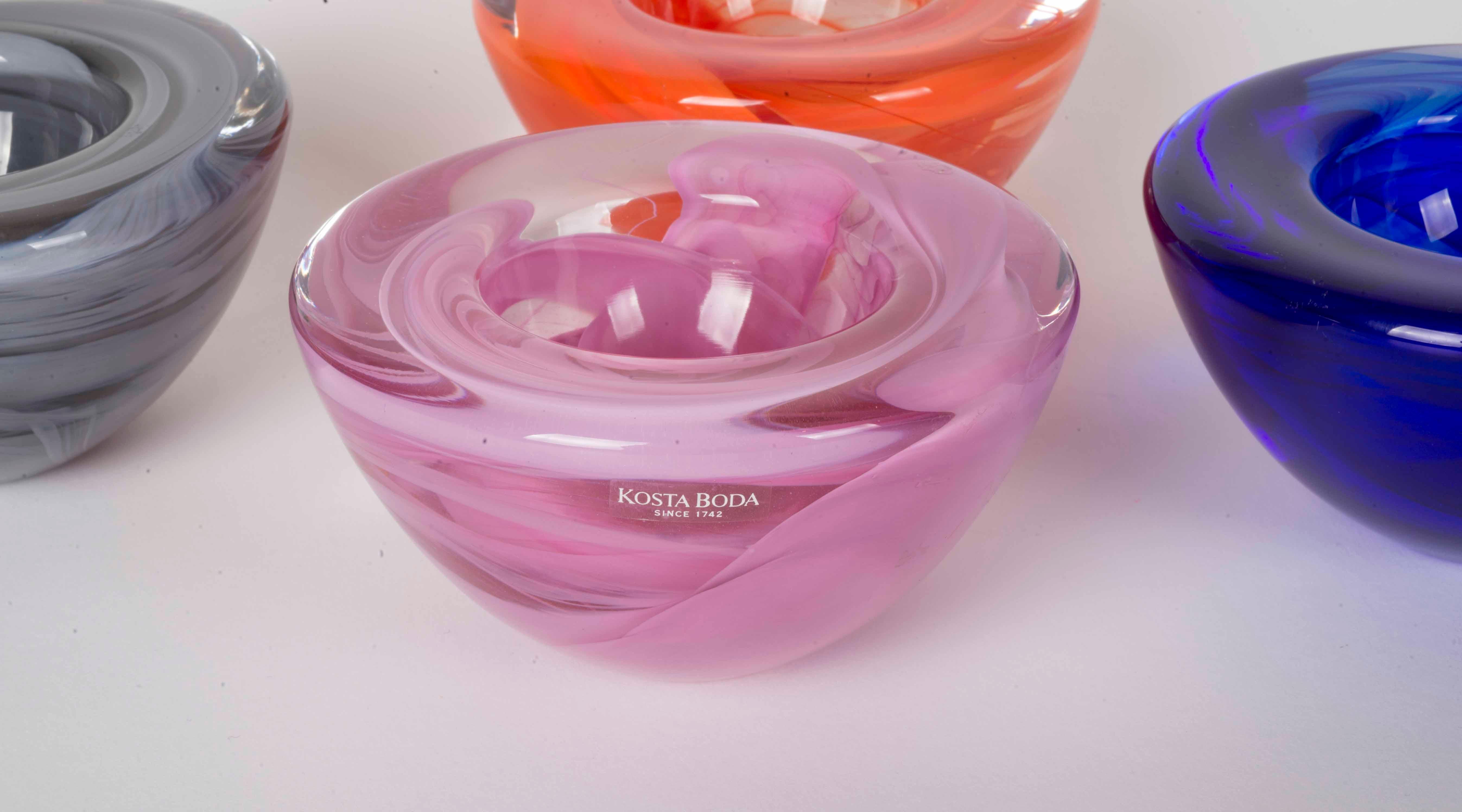 4 Kosta Boda bowls in different colors, orange, pink, blue and grey.
