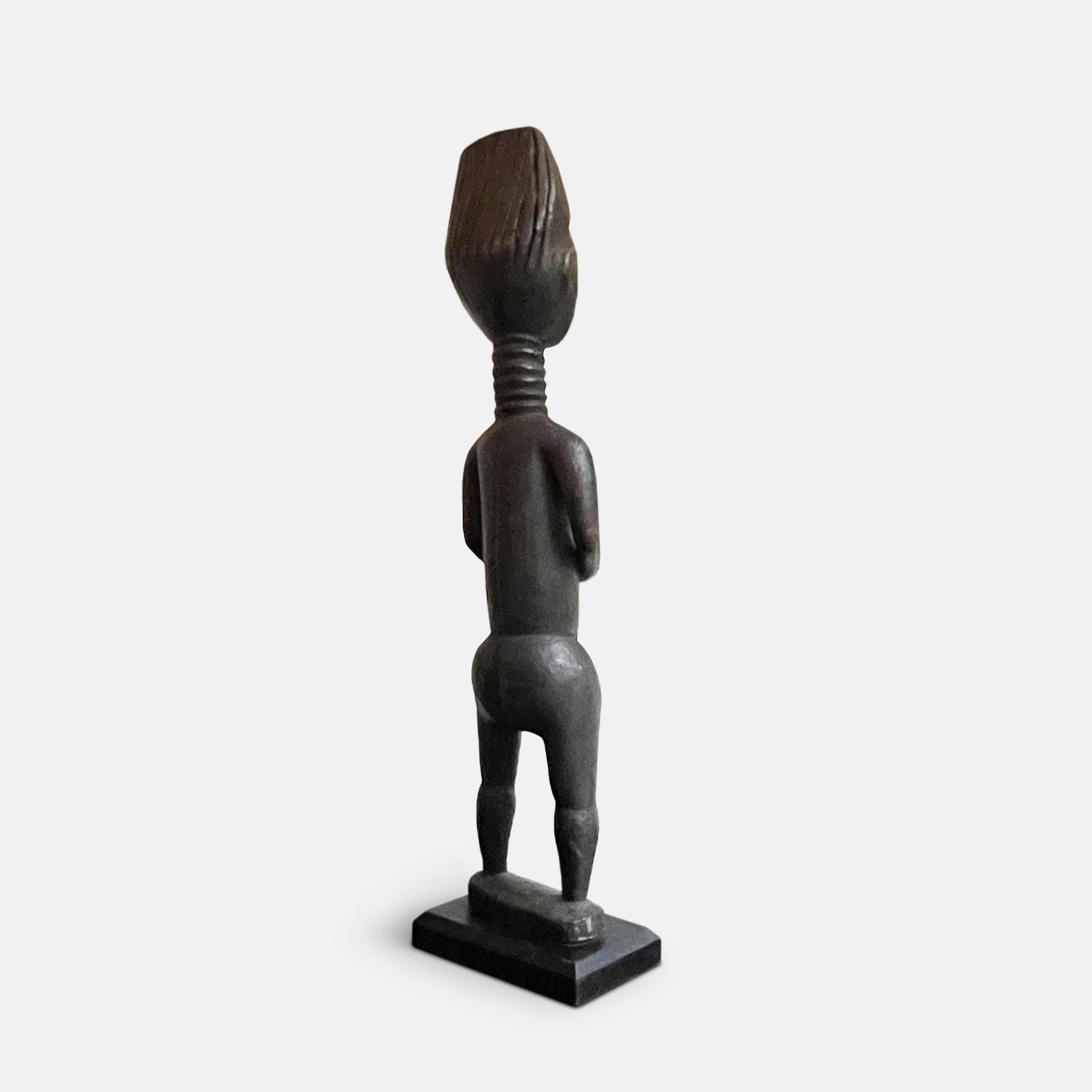 The hard wood of this female Koulango statue, from the Ivory Coast in the early 20th century, has developed a beautiful black patina. With hands resting on the abdomen, and the neck ringed, as is common in Koulango art, the pose and the face of the