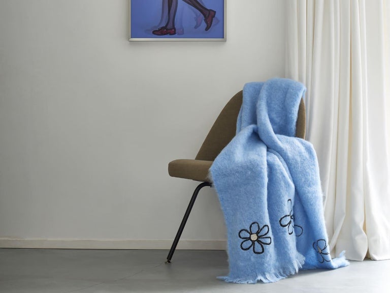 Kowhai, an elegant sweet blue throw blanket made of the finest New Zealand mohair. Adorned with flowers in black and silver skillfully embroidered by hand. A tone-on-tone fringe runs along the border. 
 
Based in the Netherlands and India's Uttar