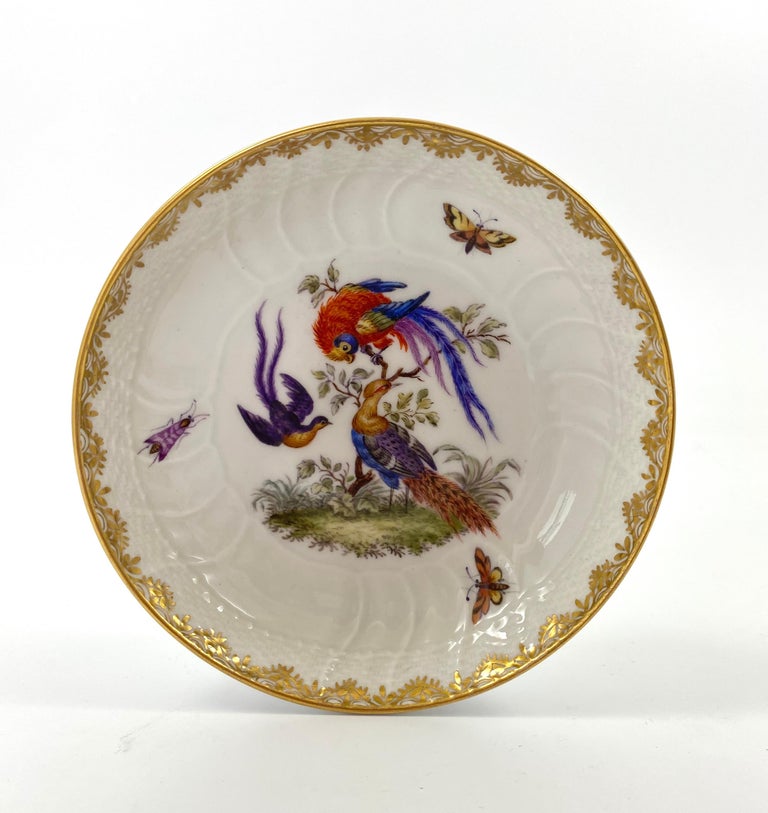 KPM Berlin porcelain cup and saucer, c. 1870. The spirally moulded cup finely and exuberantly hand painted with a group of three chickens and butterflies, beneath a gilt swagged rim. Having an elaborate branch handle, terminating in moulded leaves