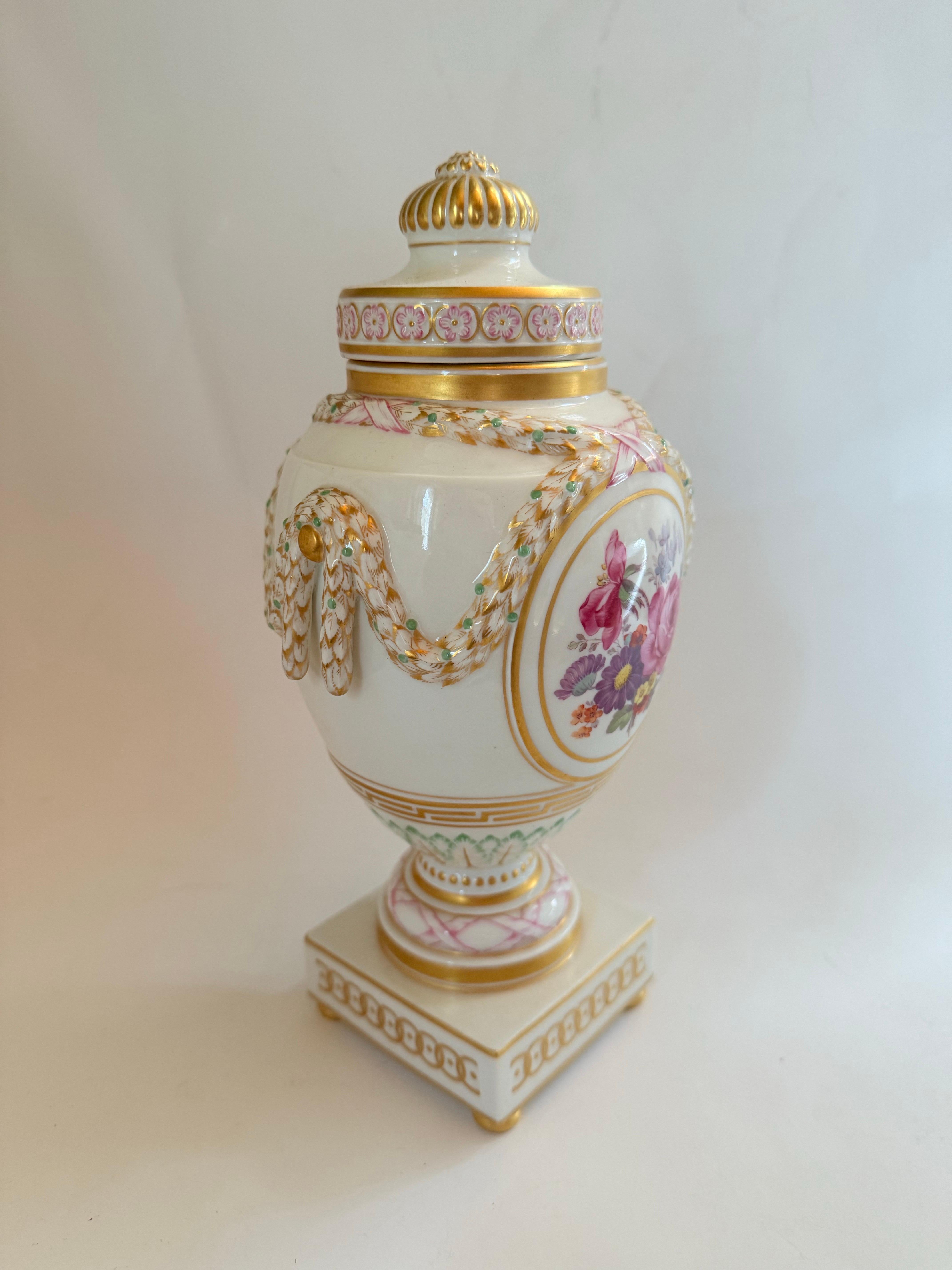 A Classic lidded vase, KPM Berlin, mark 1960-1970 1st choice, red imperial orb mark. 
Urn form on a square base with four pressed ball feet, relief decoration of ornamental friezes and surrounding laurel festoons, oval gold-framed medallion on both