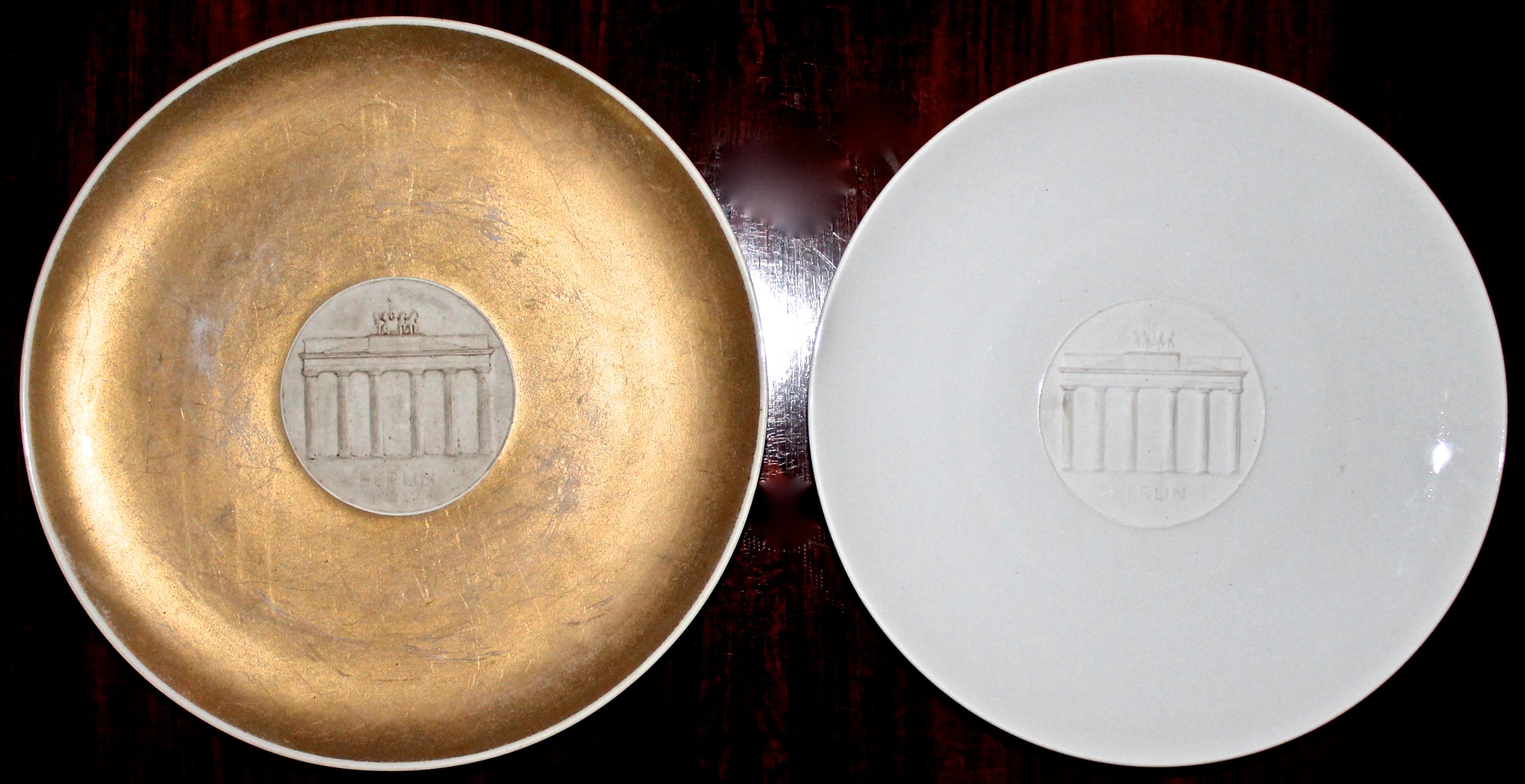 Rare period plates issued by KPM Porcelain in celebration of the infamous Nazi Olympics in 1936. Fully signed on bottom. Gold plate is slightly larger: 26.5cm x 2.5cm. The white plate is 4.8cm x 3cm. Both have holes on the back for wall hanging.