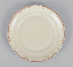 KPM, Poland. Set of nine cream-colored porcelain plates with gold decoration.