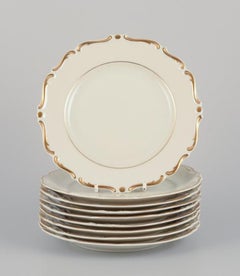 KPM, Poland. Set of nine cream-colored porcelain plates with gold decoration. 