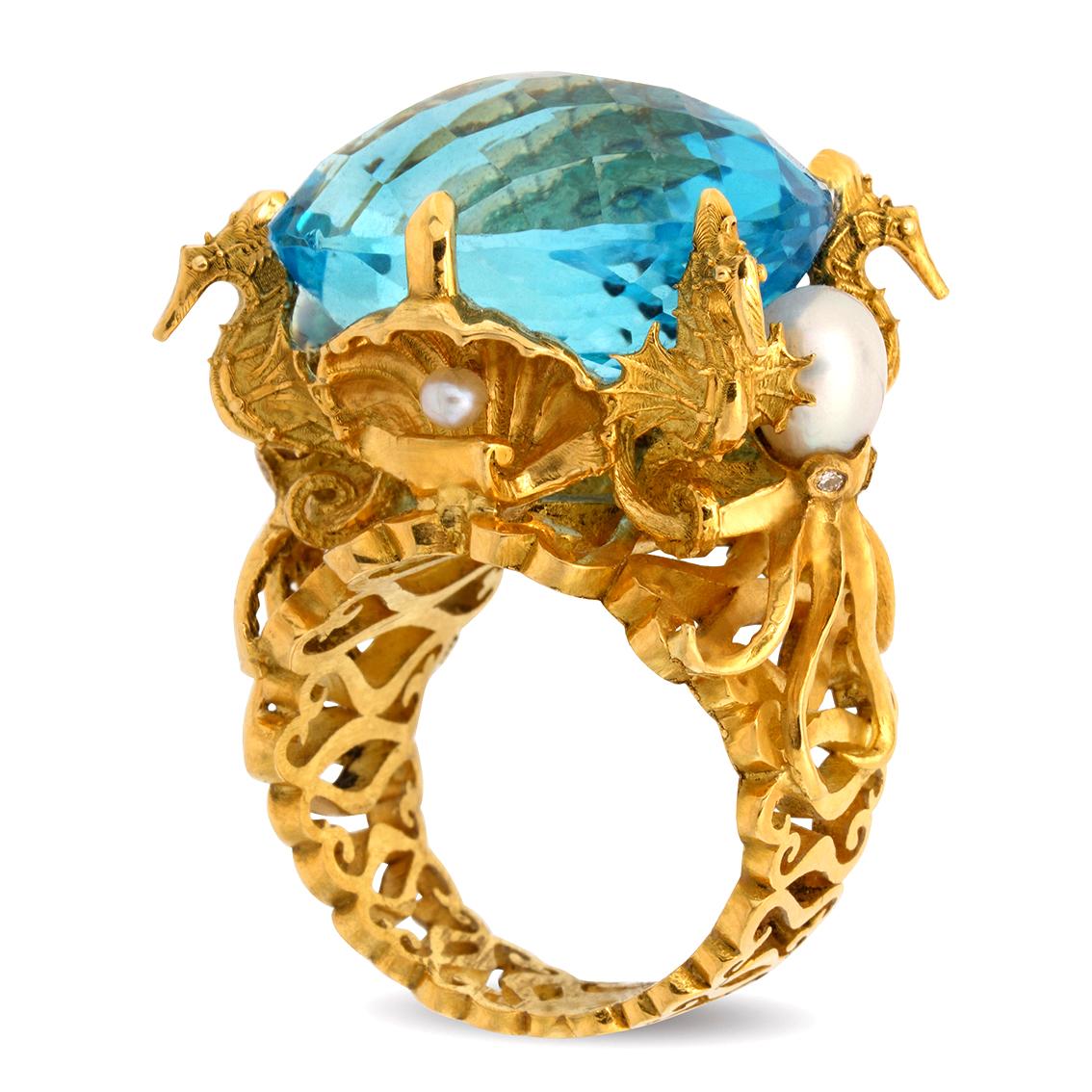 Handcrafted in 18kt yellow gold this captivating ring features a spectacular 35.3ct, 22mm x 17mm x 14mm Swiss blue oval checkerboard cut topaz buoyed upon golden seashells and flanked by four sentinel seahorses and two octopi. It features four