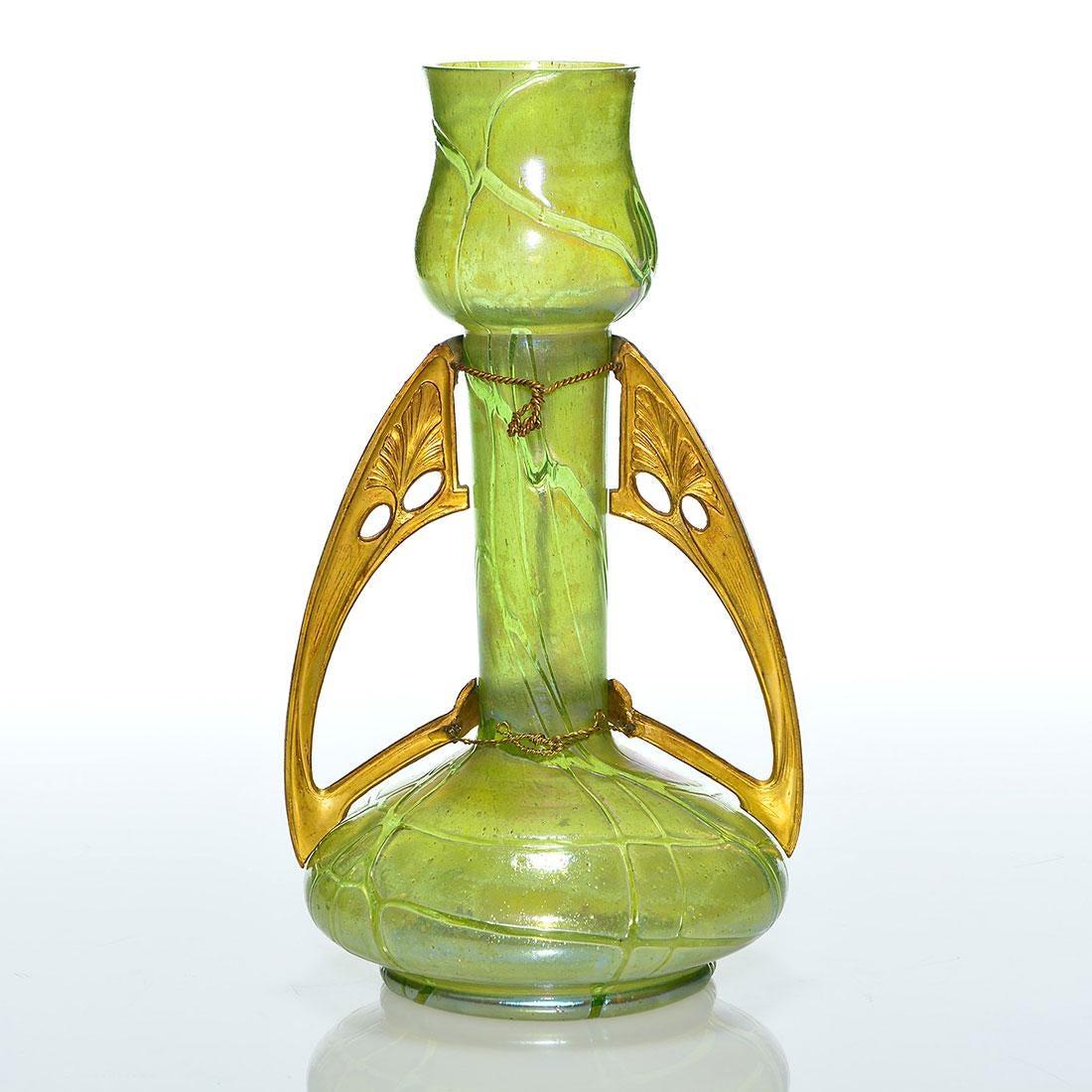A Loetz-style Art Nouveau glass vase with a gilt metal mount dating circa 1900. The design from Kralik Glassworks (Wilhelm Kralik Söhn) features a flaring tulip shaped top over a slender neck of pale, sage green glass with metallic shades of gold,