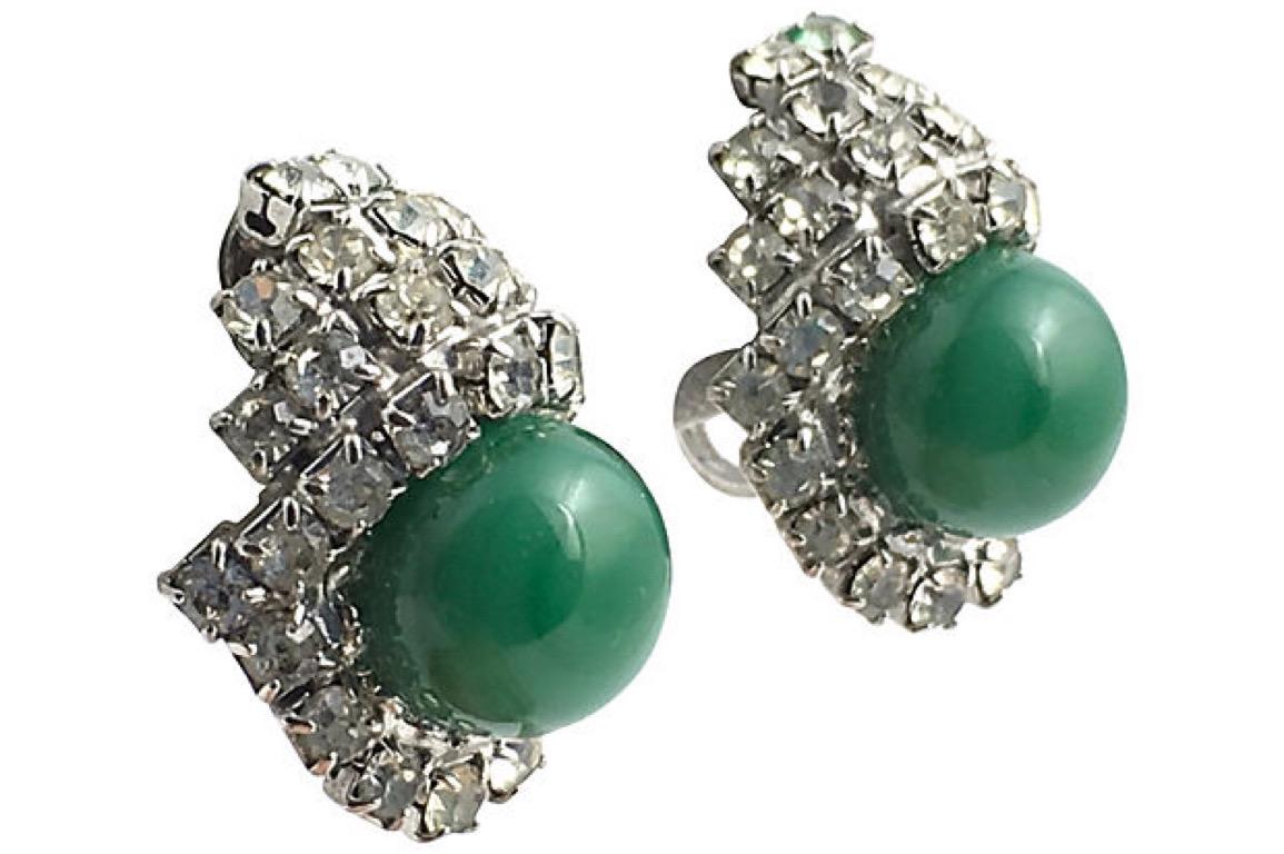Kramer clip-back earrings featuring prong-set clear rhinestones surrounding a green glass bead that resembles jade or malachite.  The stones are set in white metal. Kramer oval tag attached to the back of one earring. Age wear, slight tarnish.