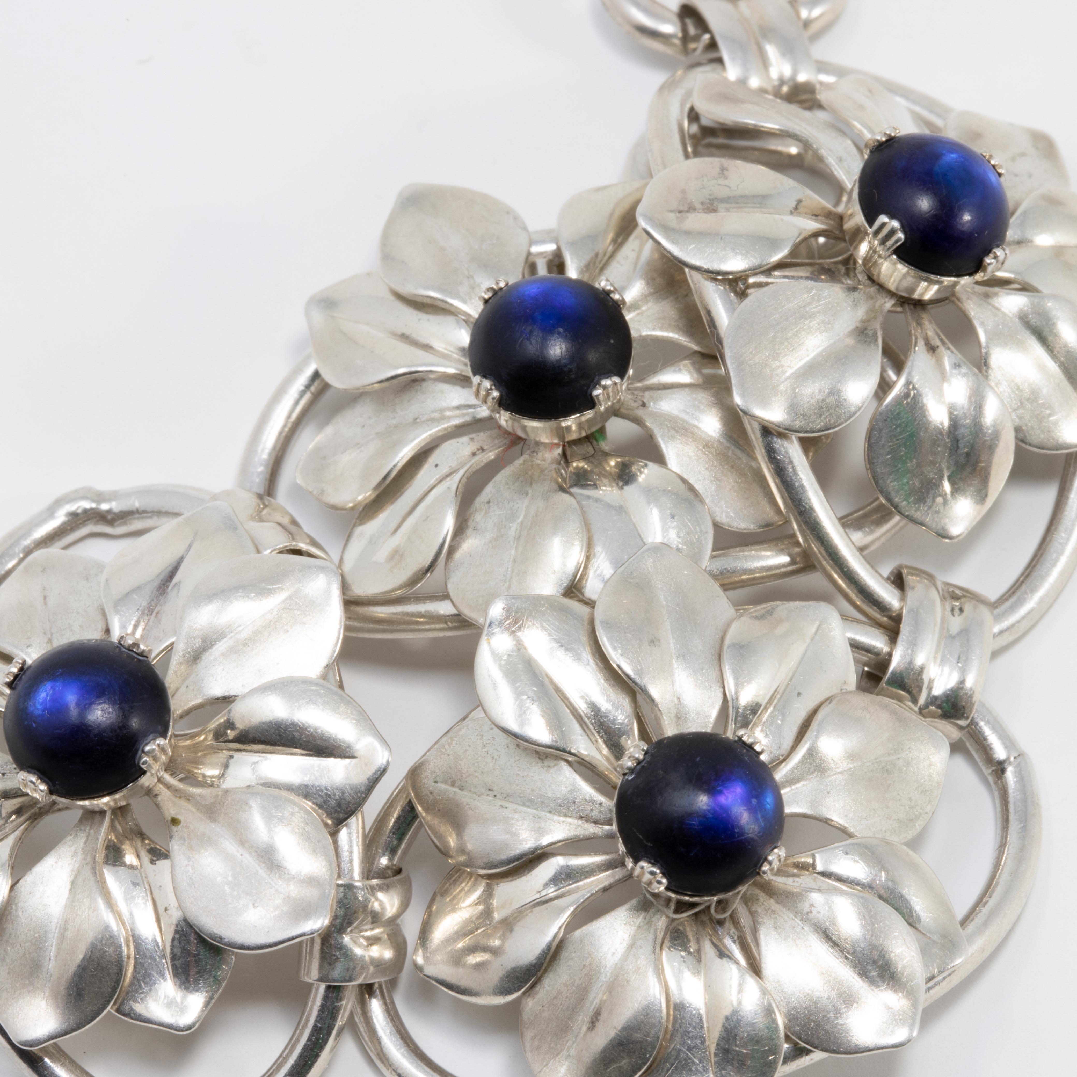 A stylish vintage bracelet. This pretty accessory features four flower links, each with a single dark blue/indigo gemstone. Fastened with a foldover clasp.

Hallmarked: Kreisler Sterling

