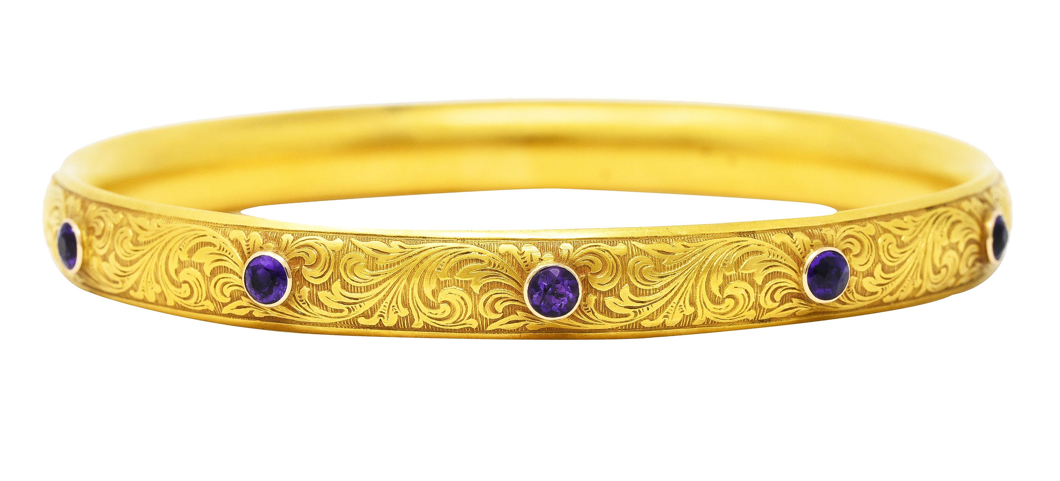 Bangle bracelet features a raised scrolled whiplash motif atop an engraved linear texture. Featuring five bezel set 3.0 mm round cut amethysts. Transparent medium-dark purple in color.
Inscribed 'LEB from MJB 1908'. Stamped 14K for 14 karat gold.