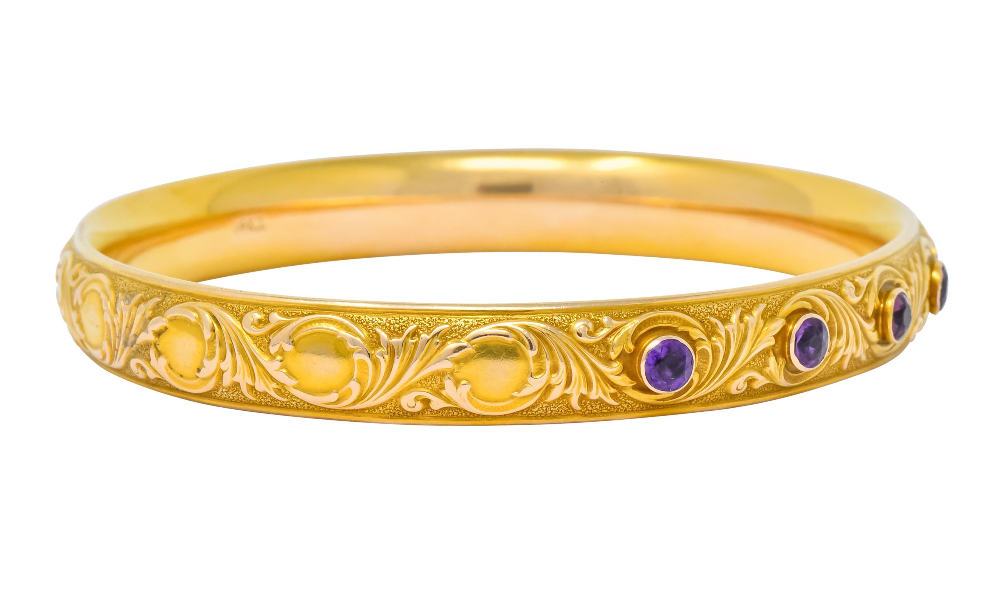Bangle style bracelet deeply engraved throughout with scrolling, foliate, whiplash motif and finished with a stippled texture

Bezel set to front with seven round cut amethysts, transparent and a vibrant orchid purple in color

With maker's mark for