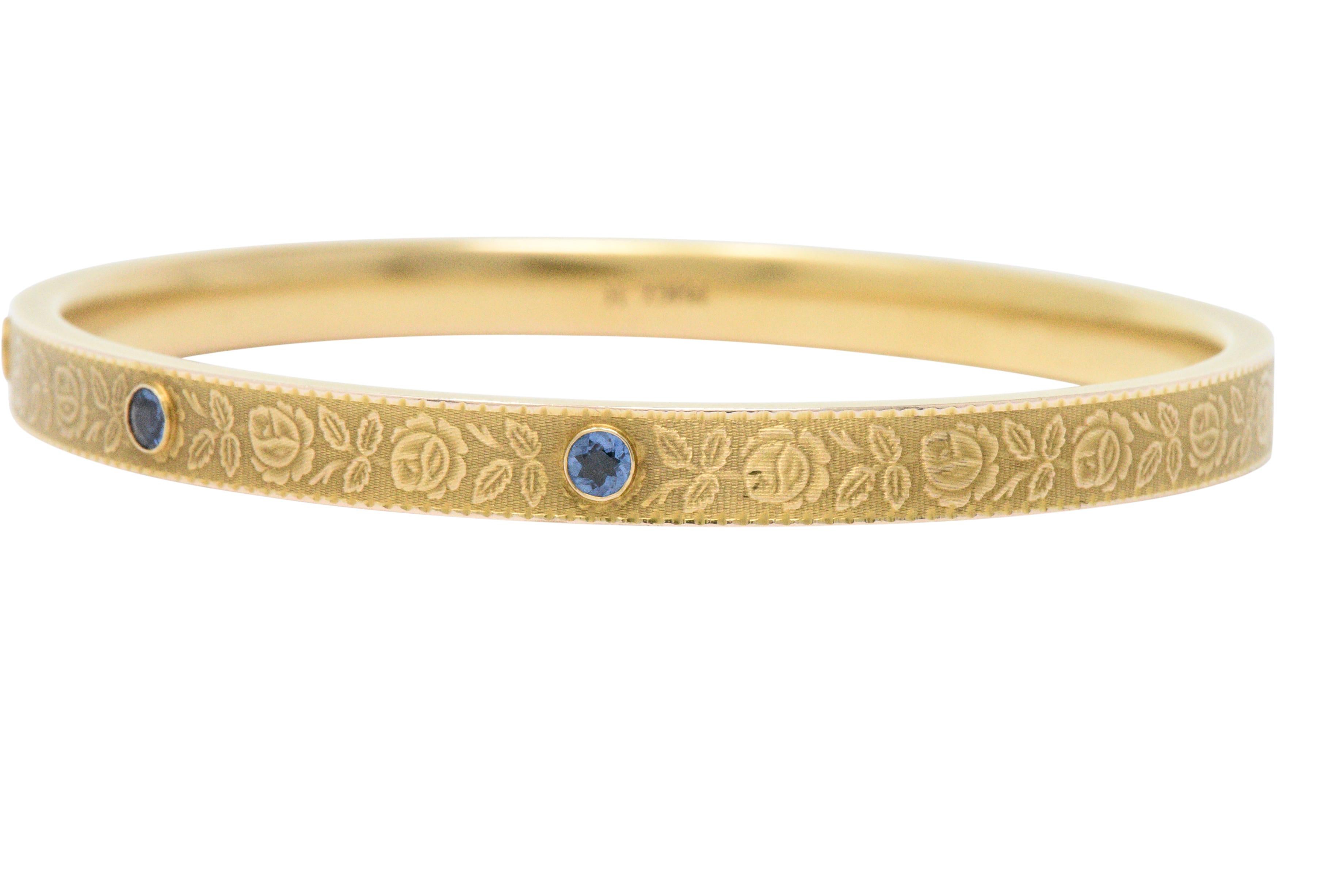 Bangle style bracelet featuring extraordinarily engraved rose and foliate motif throughout finished by a subtle texture

Bezel set to the front with three round cut sapphires weighing approximately 0.45 carat; incredibly well-matched and medium-dark