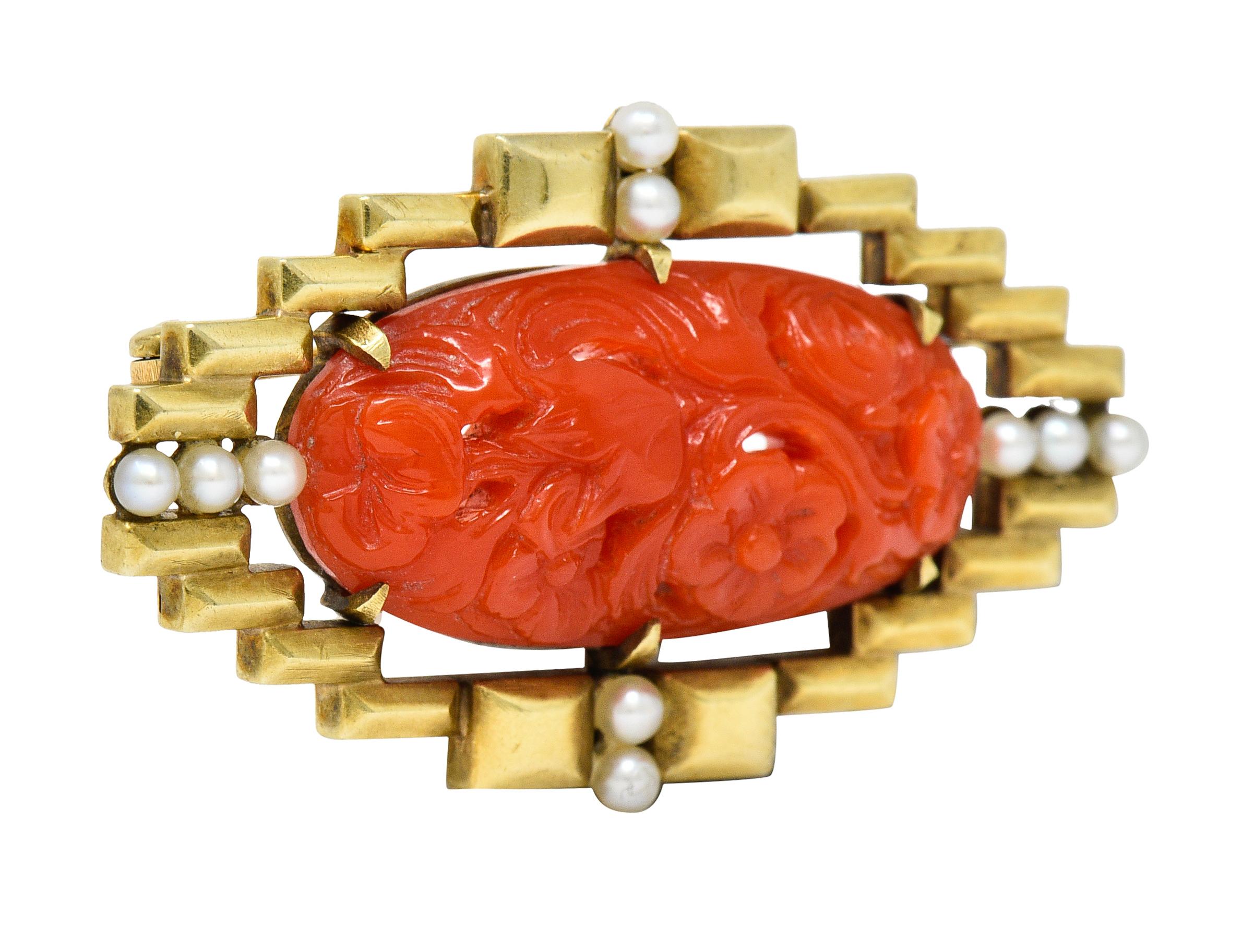 Centering an oval cabochon of coral, deeply carved to depict scrolling florals

Opaque with uniform orangey-red color and measures approximately 27.0 x 12.5 mm

Claw set with a geometric surround accented by 2.5 mm round pearls

Well-matched with