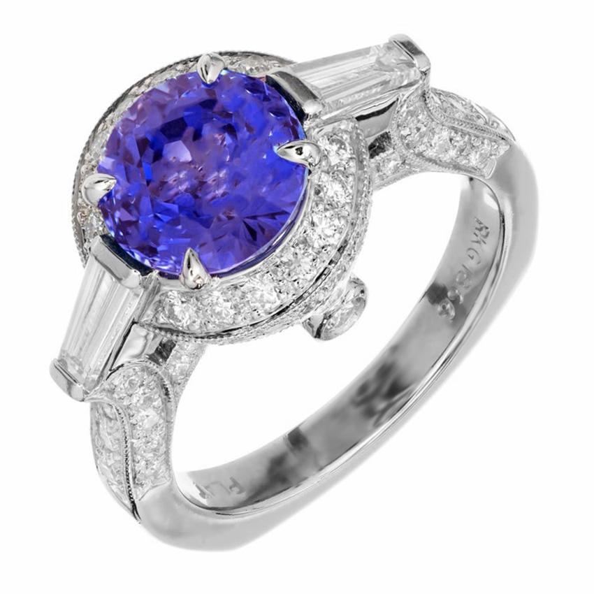 Cornflower blue sapphire and diamond three-stone engagement ring by classic designer, Krementz. 3.57ct cornflower blue round Sapphire center stone. Mounted in a Platinum setting, accented with a baguette diamond on each side of the stone as well as
