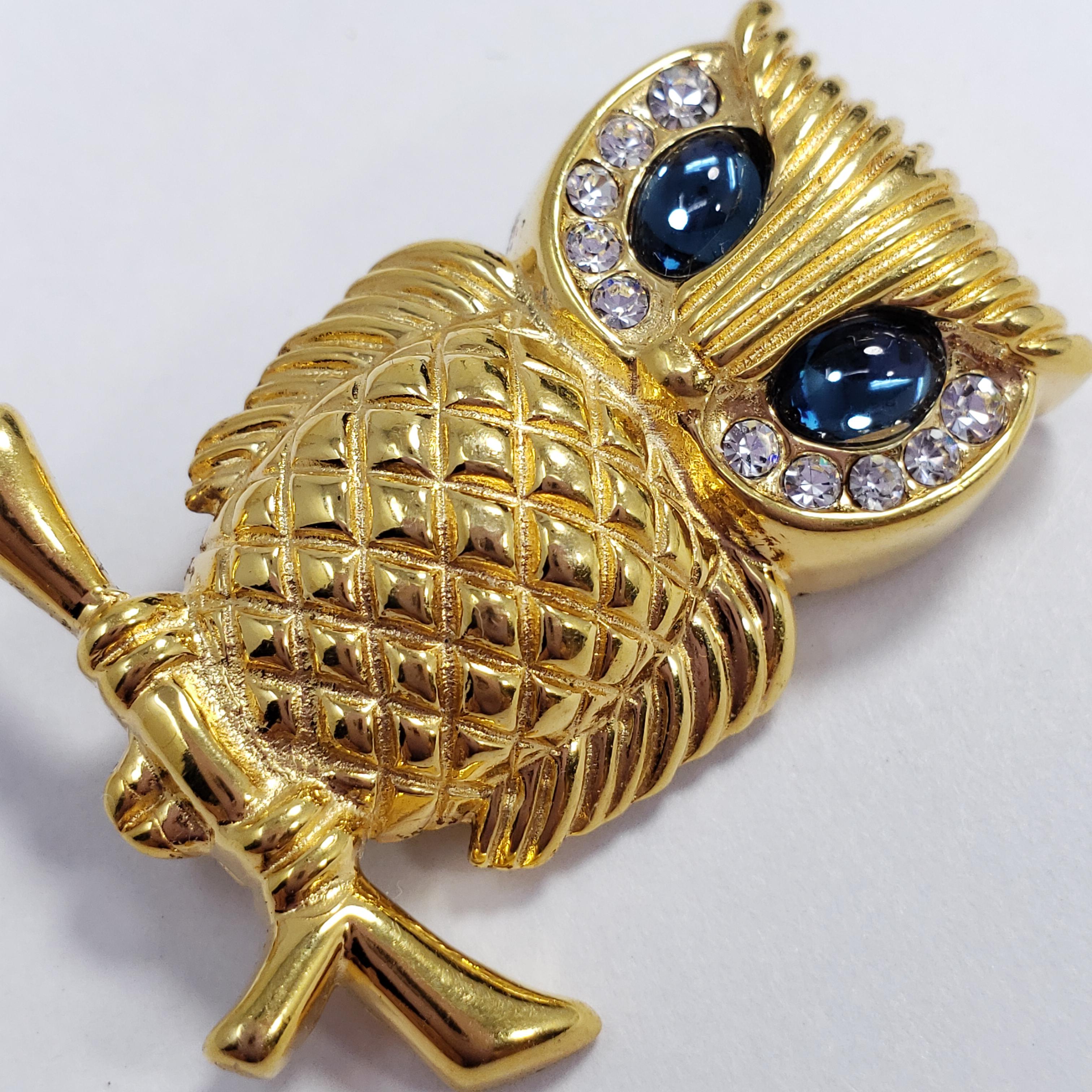 A vintage pin brooch by Krementz & Co. A gold-filled owl is perched atop a branch, its head accented with two opaque sapphire-colored cabochons and clear crystals.

Hallmarks: Krementz (on pin stem)
