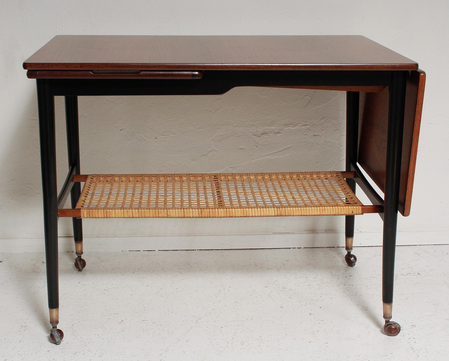 It's a side table, a coffee table, a serving table - it's a beautifully restored Danish walnut and rattan drop-leaf host/Hostess table with slide-out stainless steel serving tray, black painted legs, and brass sabots, by Kresten Buch, circa 1960.