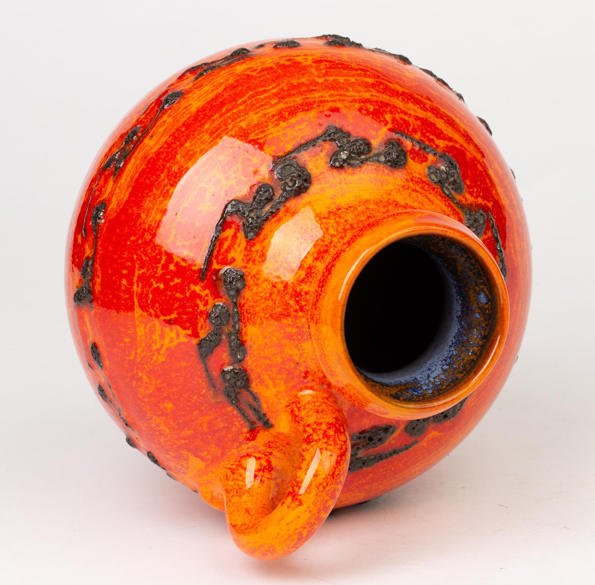 Un étonnant vase à anse en poterie d'art allemande du milieu du siècle, décoré de glaçures rouges/oranges vibrantes avec des motifs de lave noire par Kreutz Keramik. Le vase en poterie repose sur un pied étroit et arrondi, avec un corps de forme