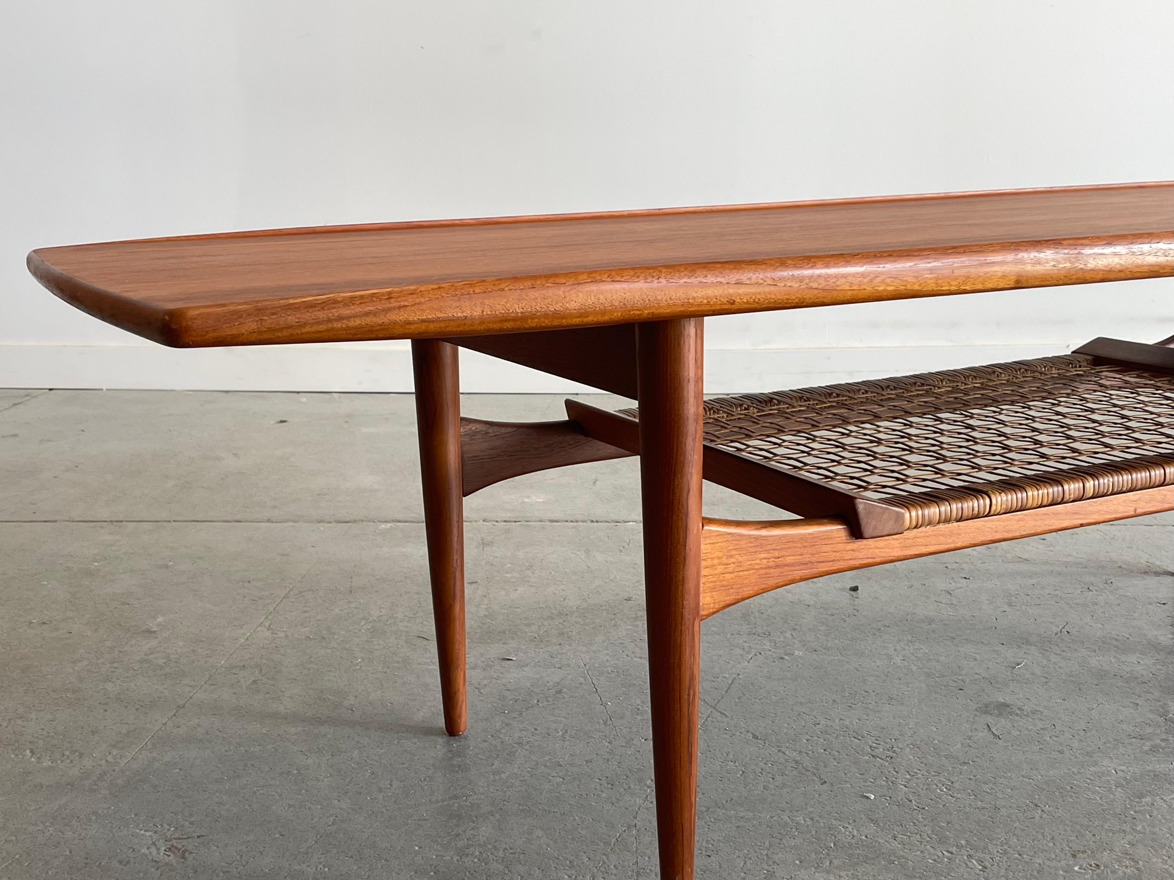 Beautiful Danish teak coffee table by Kristiansen & Thomassen, Denmark. This striking piece features nicely sculpted edging and woven cane shelf. Measures 63” W x 22” D x 18” H. Nice restored condition with minor age-appropriate wear. 