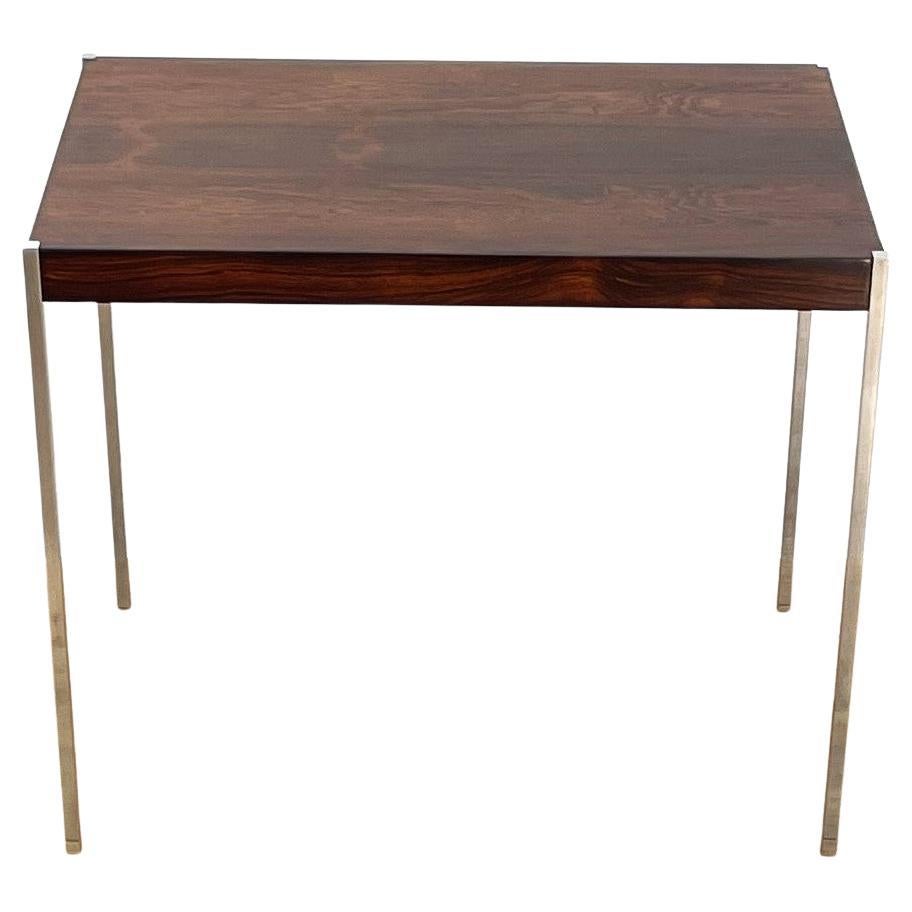 Tavolino Kristiansson per Luxus. Con il suo design elegante in cui la leggerissima struttura metallica mette in risalto le venature e il calore del palissandro, questo tavolo è raffinato ed elegante. Questo modello è l'esempio perfetto di come i