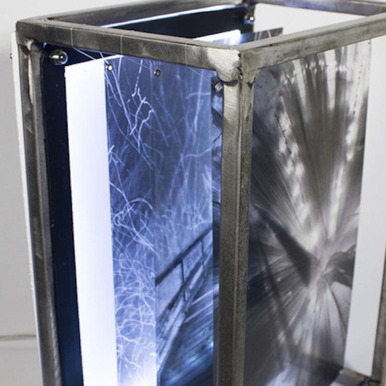 Lacy Pathways is a mixed media light box comprised of steel and pigment prints. This particular light box combines three images that alter the viewer’s sense of reality; a staircase seems to descend into nothing, surrounded by an excessive amount of