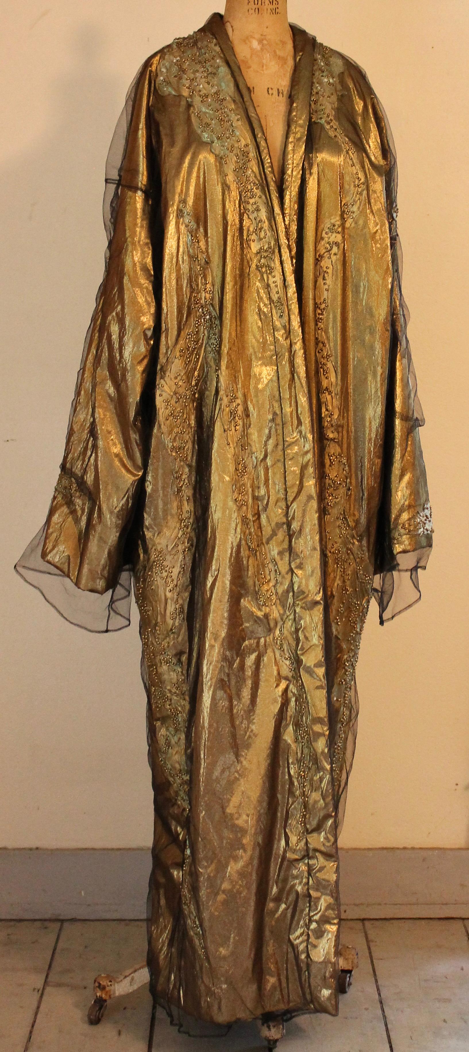 Gold lame, under a layer of transparent fine black gauze, hand worked abstract curved strokes (front, back. and sleeves) with a metallic paint (with a slight blue oxidation) and faux faceted beads within. Total effect is very Fortuny.