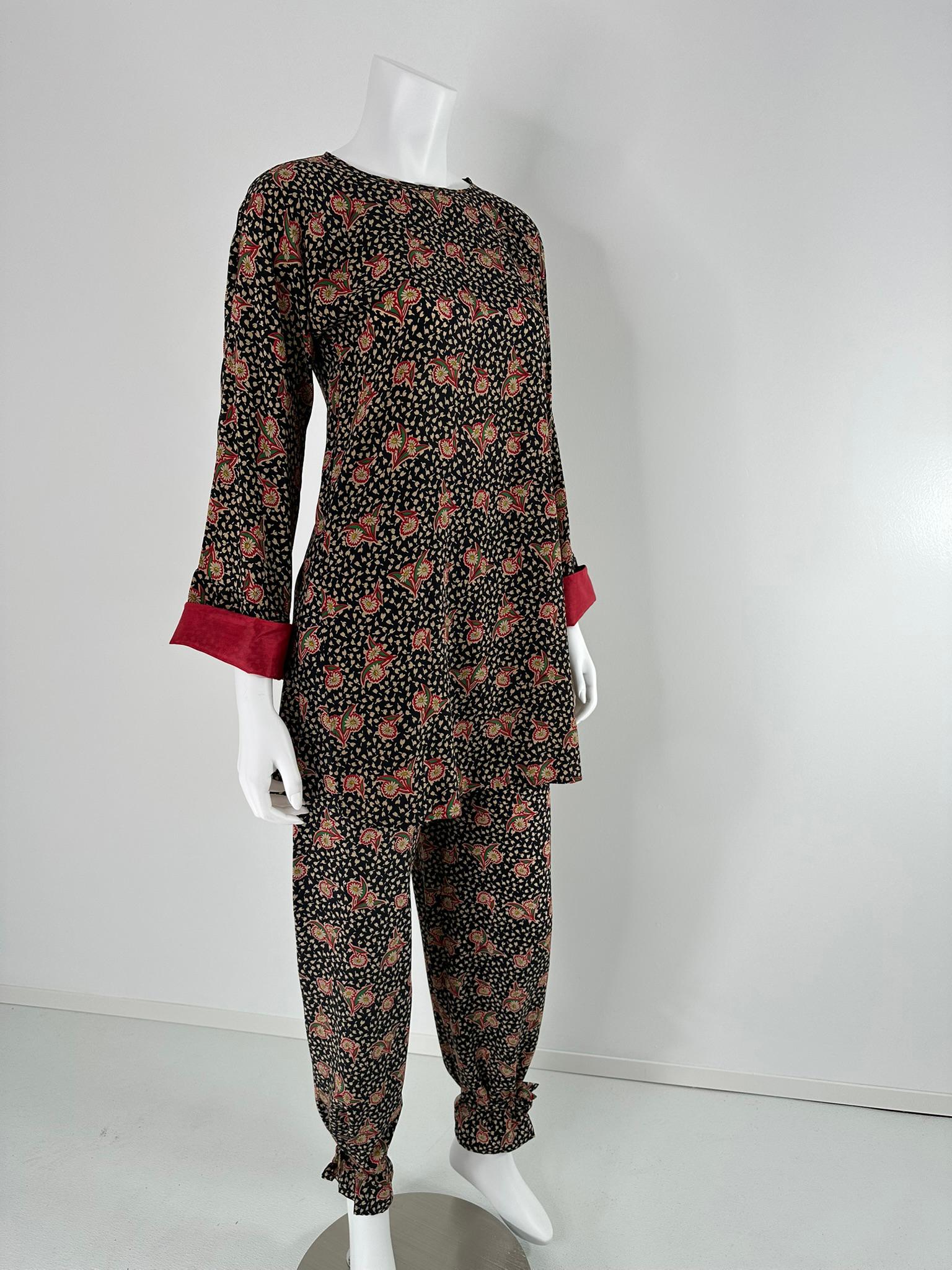 Krizia, tunica in seta con stampa floreale e pantalone con lacci alla caviglia degli anni Ottanta. La casacca nera con foglie color crema e stampa floreale rossa e verde ha una chiusura a scatto singola sulla spalla sinistra. Maniche lunghe e piene