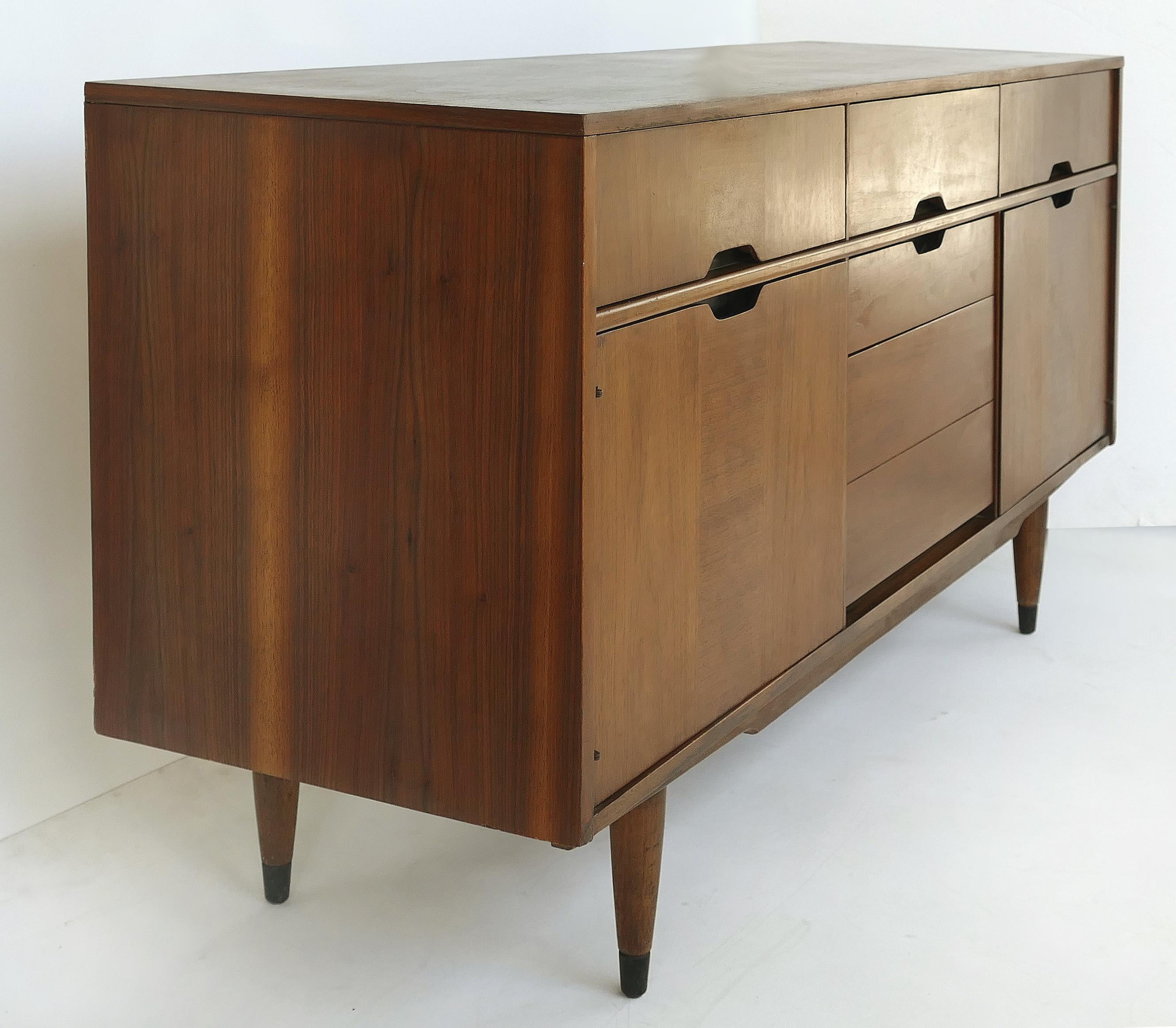 Offered for sale is a Kroehler custom crafted Mid-Century Modern credenza. The cabinet is supported by tapered legs with brass capped feet. The center portion has three drawers with the bottom drawer being doubled in depth. The credenza has drawers